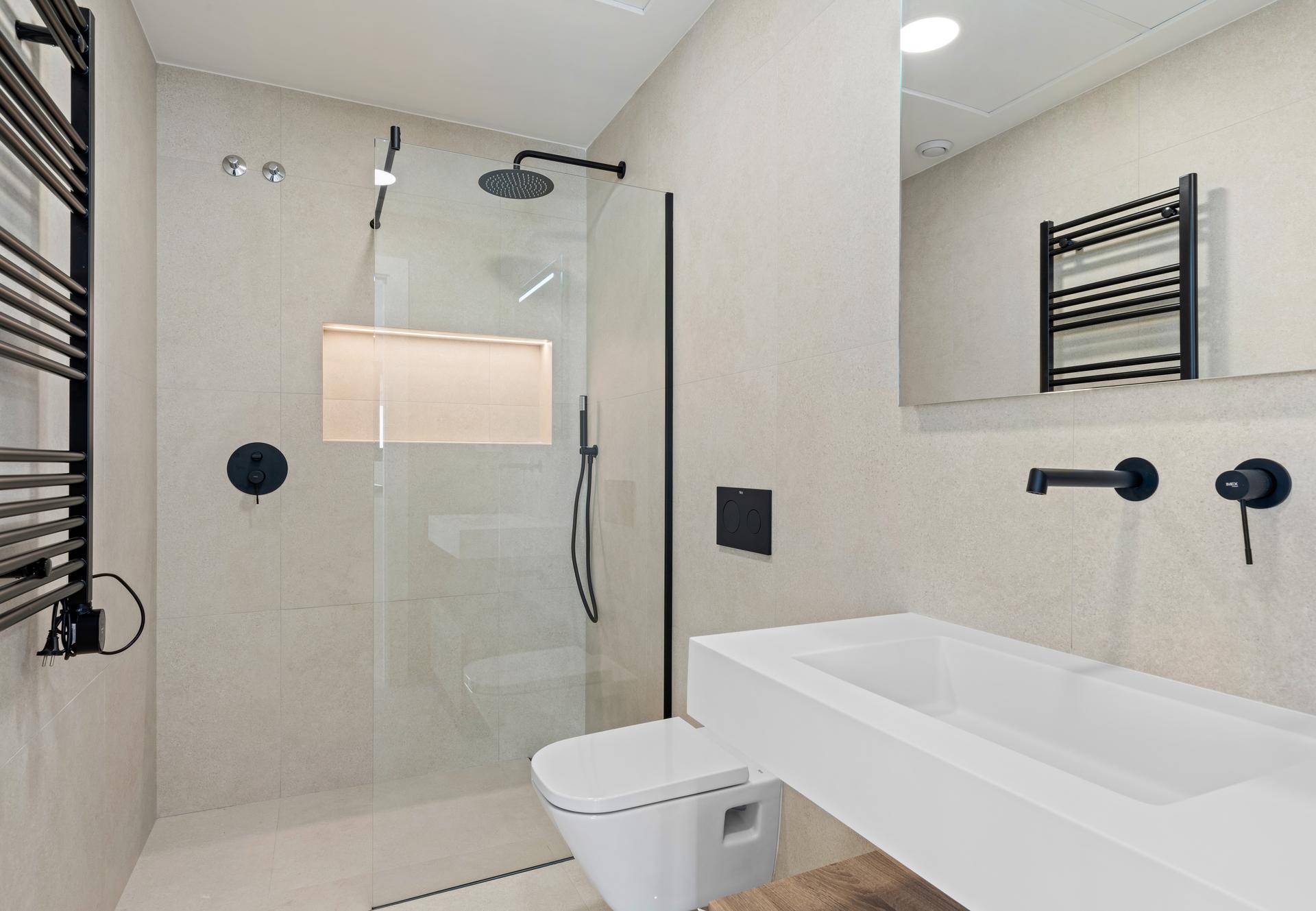 Modernes Badezimmer mit begehbarer Dusche, wandhängendem WC, beheiztem Handtuchhalter und eleganten Fliesen.