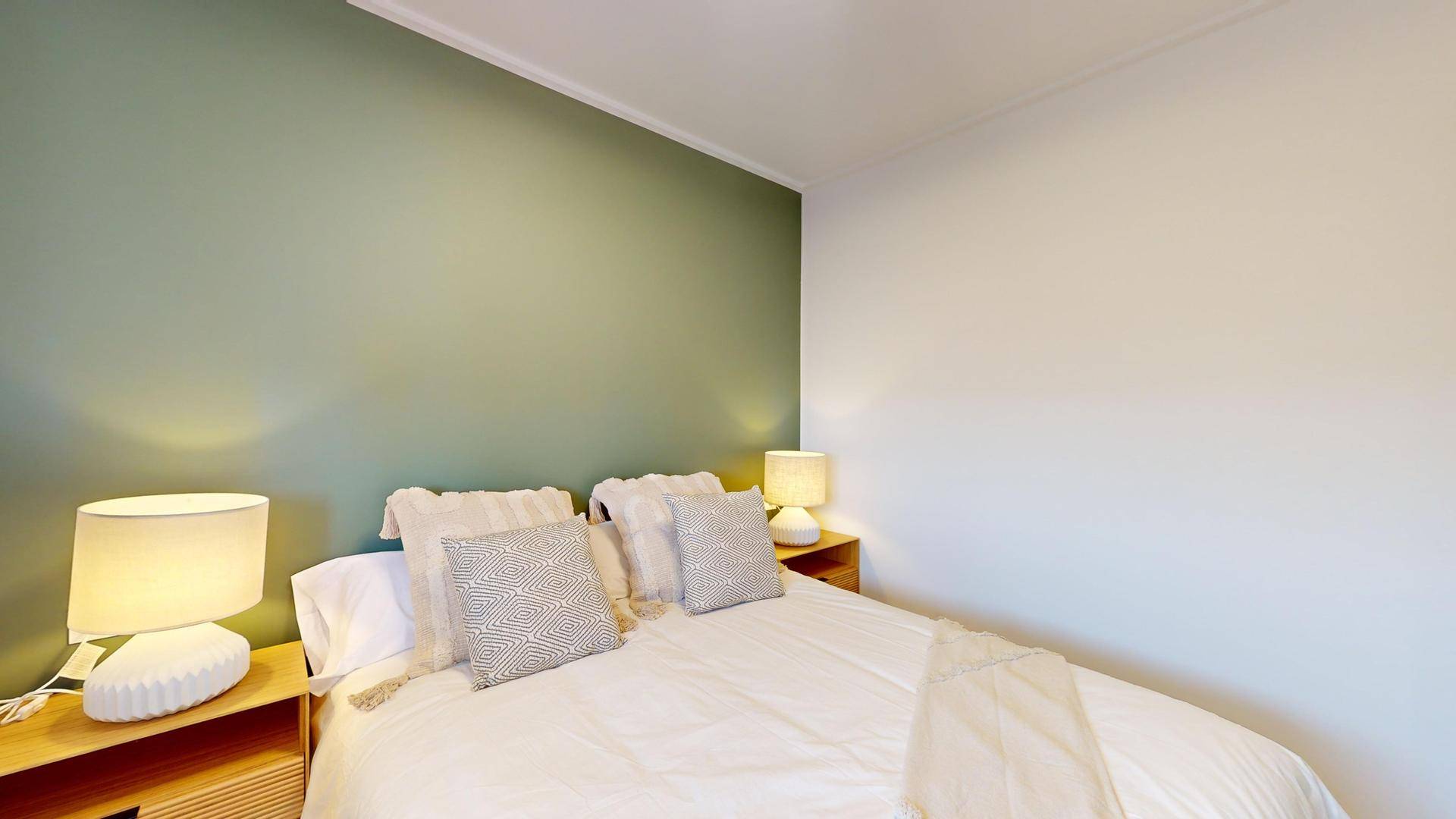 Schlafzimmer mit Doppelbett und einer Akzentwand in beruhigendem Grünton.
