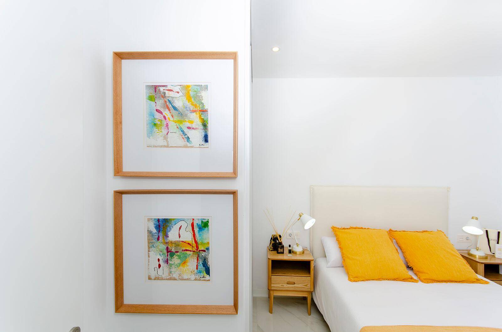 Helles Schlafzimmer mit Doppelbett, Nachttischen und farbenfrohen Bildern an der Wand.