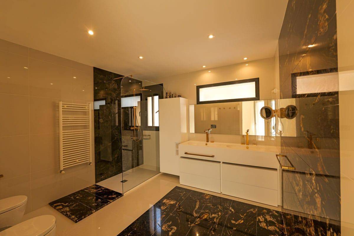 Modernes Badezimmer mit dunklen Marmorfliesen, begehbarer Dusche und Doppelwaschbecken.