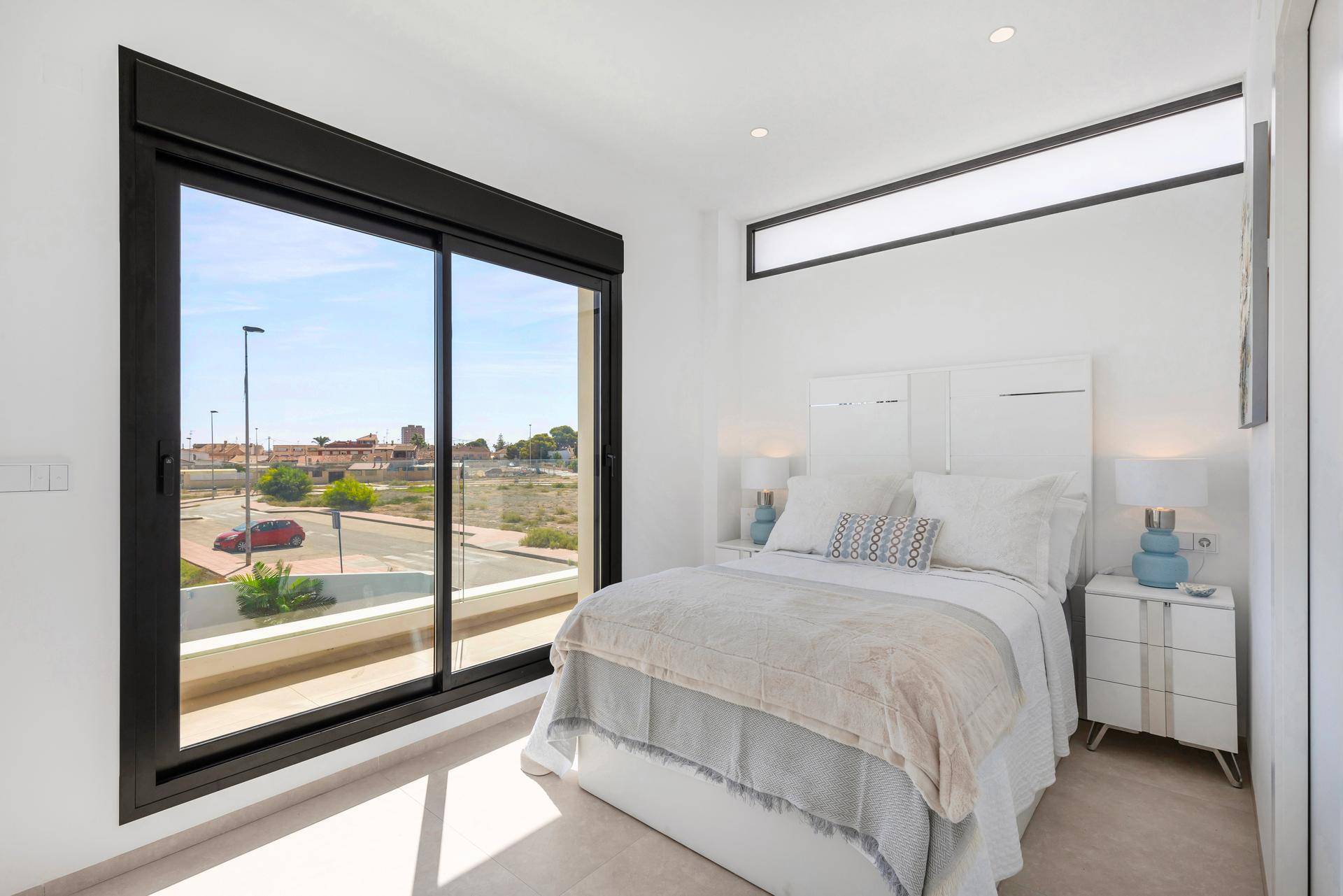 Helles Schlafzimmer mit großem Fenster, das viel Tageslicht hereinlässt und Blick auf die Straße bietet.