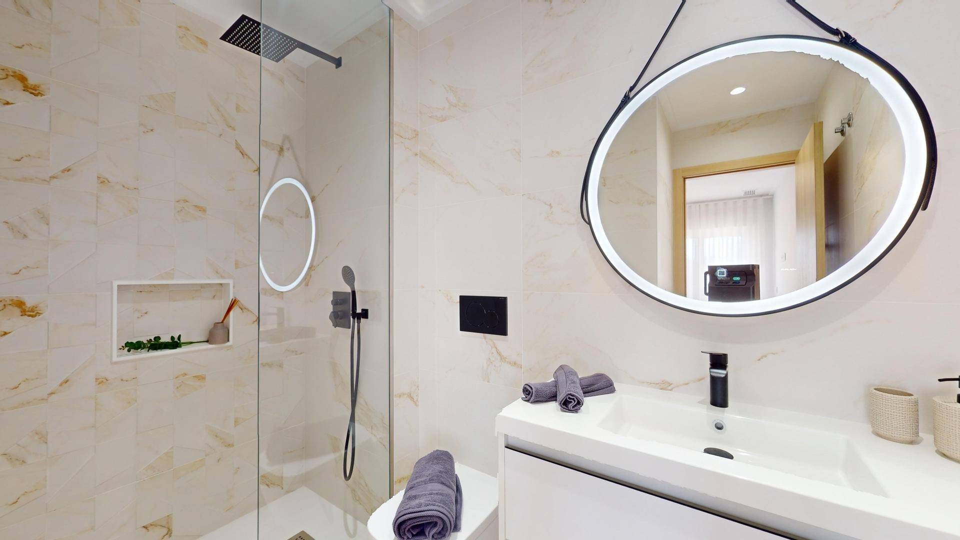 Elegantes Badezimmer mit Waschtisch, rundem Spiegel und einer modernen Duschkabine.