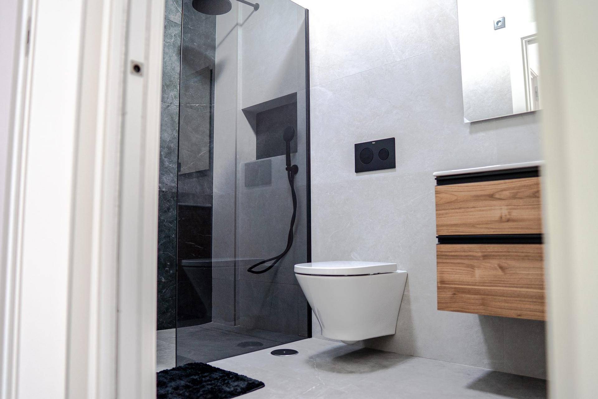 Modernes Badezimmer mit wandhängendem WC, begehbarer Dusche und Holzwaschtisch.