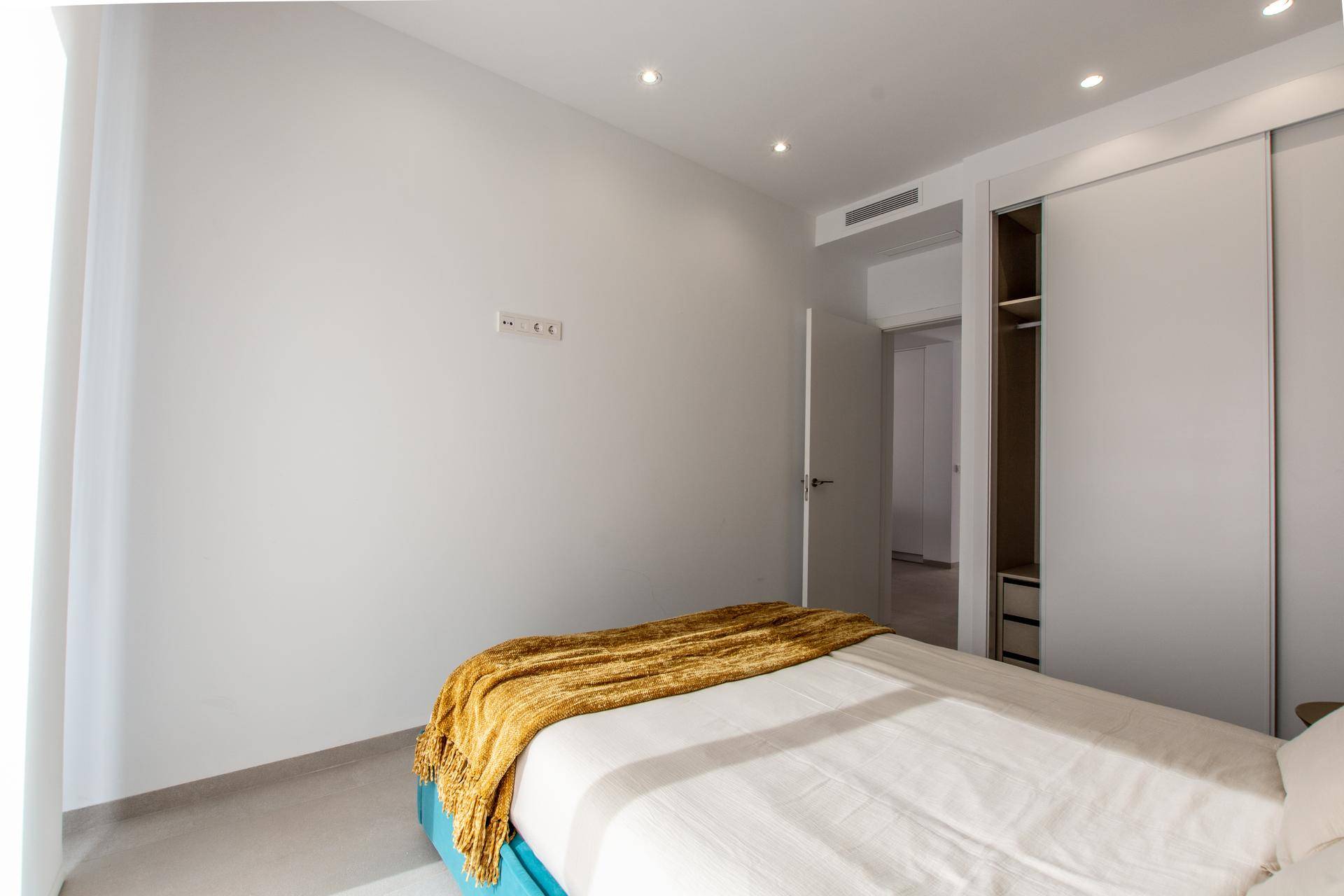 Modernes Schlafzimmer mit hellem Bett, gelber Decke und integriertem Kleiderschrank.