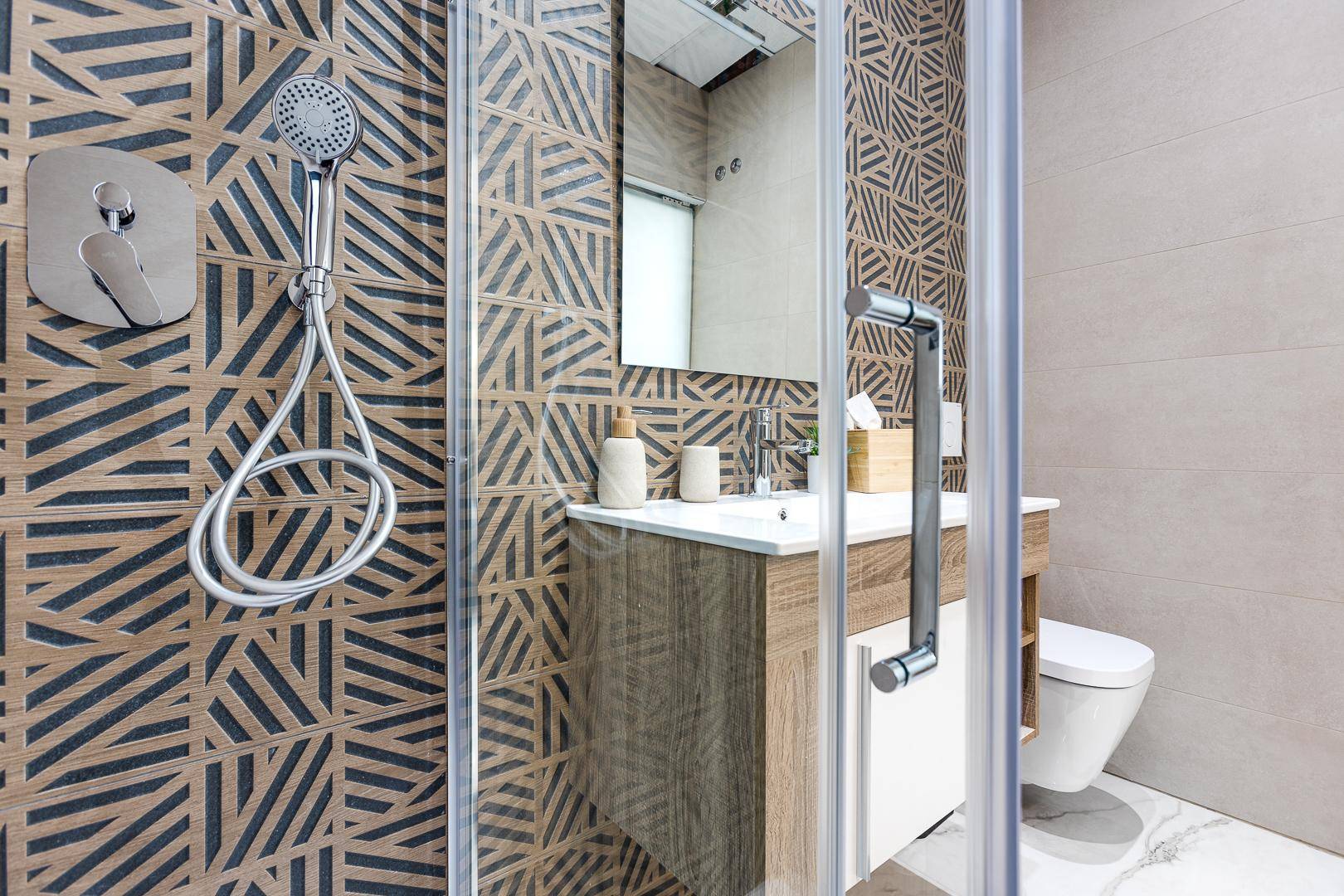Moderne Duschkabine mit geometrischen Fliesen und stilvoller Armatur im Badezimmer.