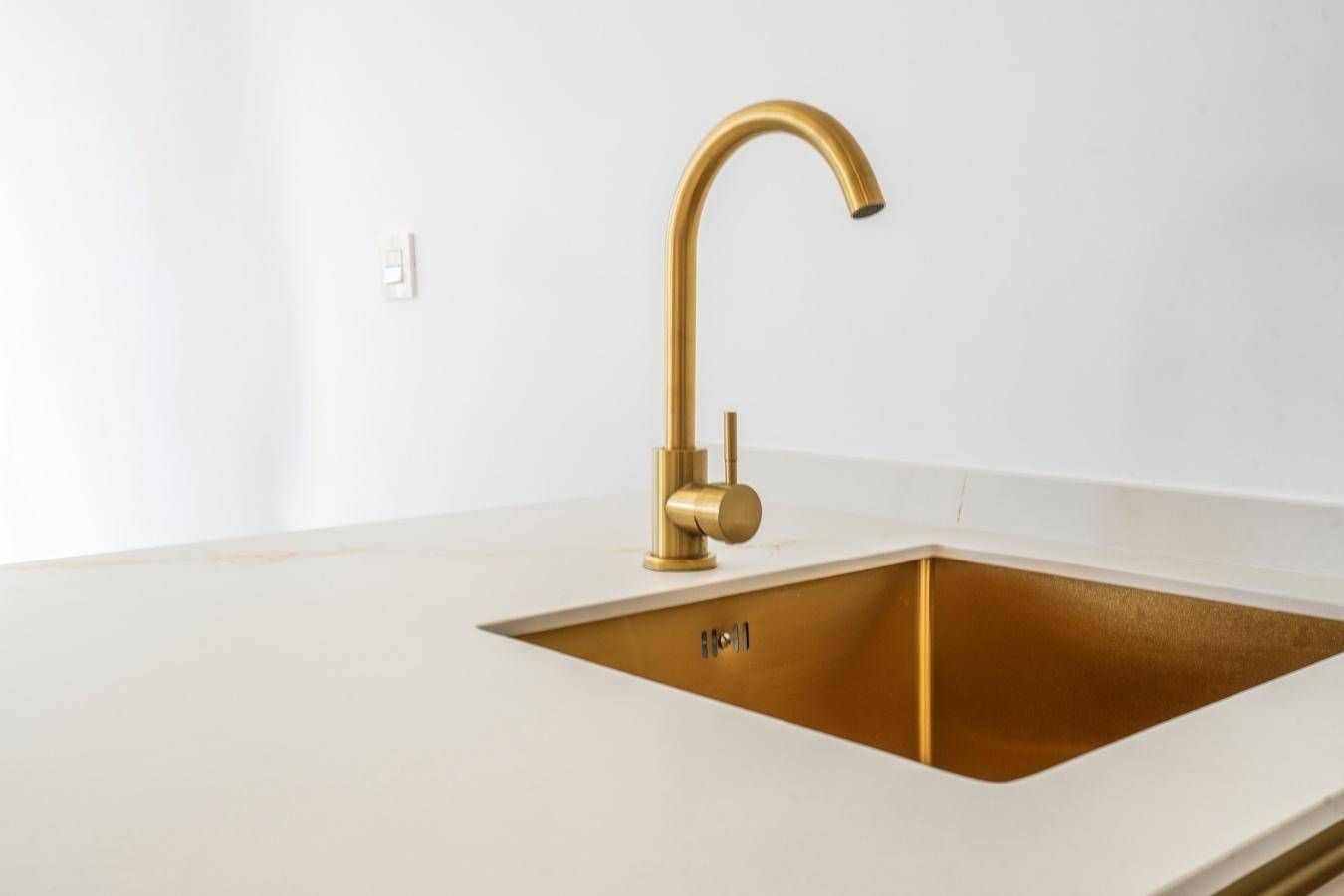 Elegante Küchenspüle mit weißer Arbeitsplatte und luxuriösen goldenen Armaturen und Spülbecken.