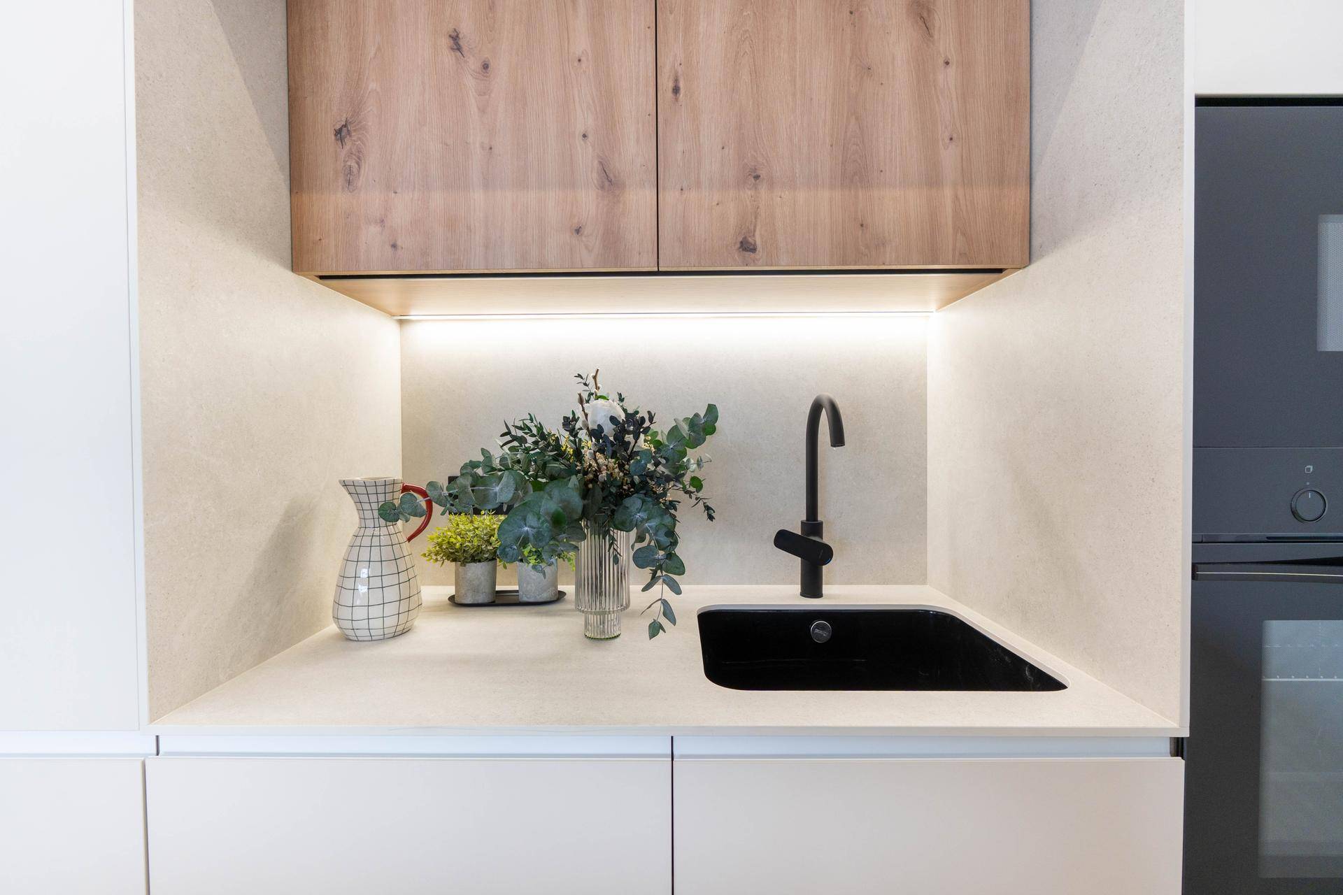 Funktionale Küchenzeile mit schwarzem Spülbecken, Holzschränken und integrierter Beleuchtung.