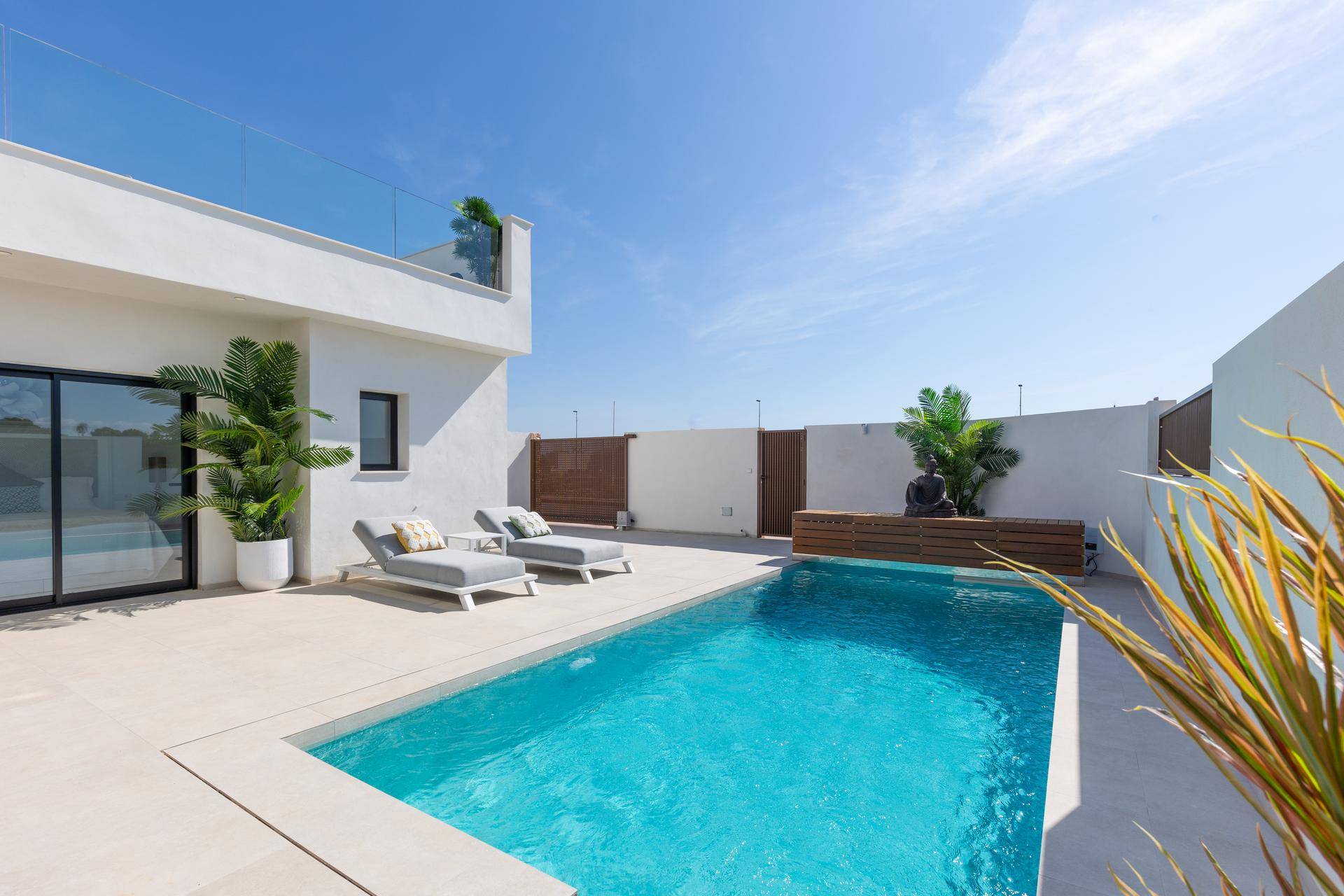 Sonniger Poolbereich mit Liegestühlen und moderner Architektur im Hintergrund.