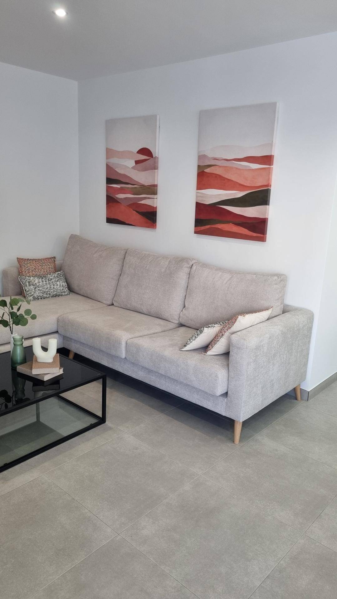 Helles Wohnzimmer mit beigem Sofa, modernen Bildern und Fliesenboden.
