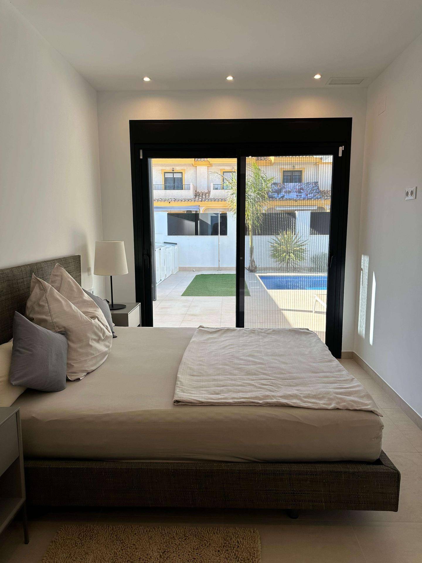 Helles Schlafzimmer mit Doppelbett und direktem Zugang zum Poolbereich im Freien.