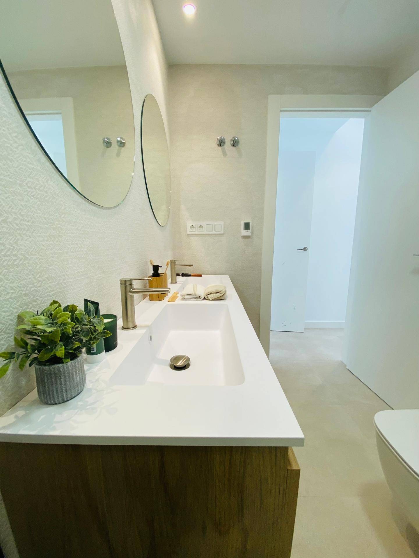 Stilvolles Badezimmer mit modernem Waschtisch, runden Spiegeln und Zugang zu einem weiteren Raum.