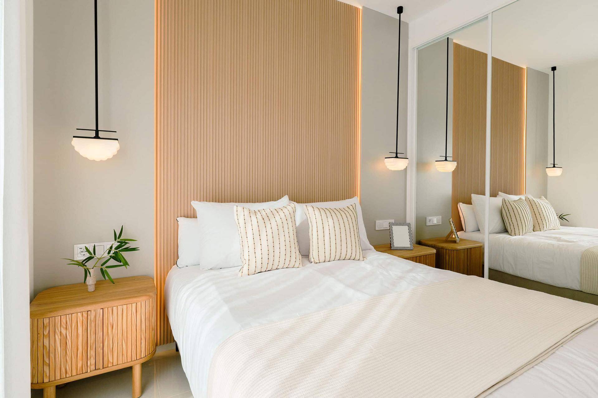Modernes Schlafzimmer mit hellem Holzpaneel als Kopfteil und minimalistischer Beleuchtung.