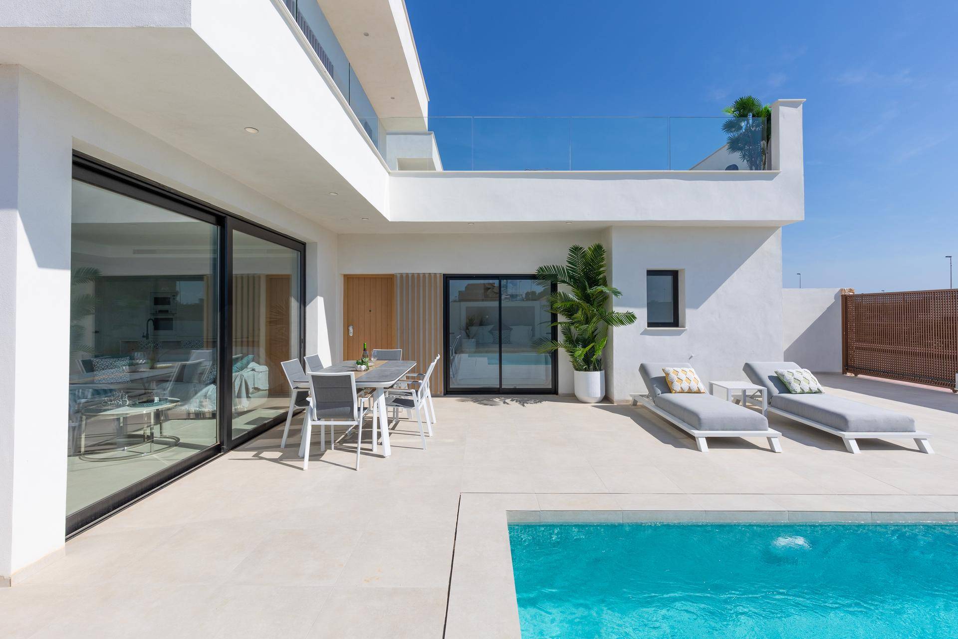 Heller Terrassenbereich mit Pool, Liegen und Esstisch vor der modernen Villa.