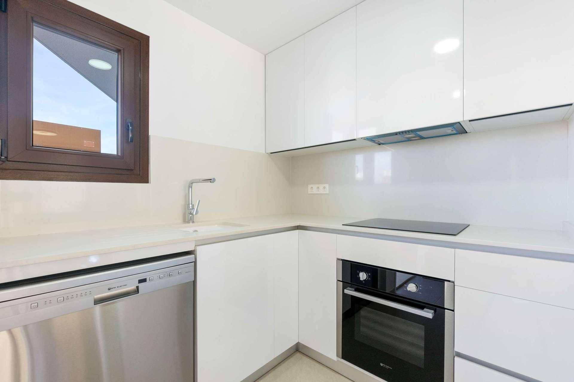 Helle Küche mit weißen Schränken, Spülmaschine, Backofen und einem Fenster für natürliches Licht.
