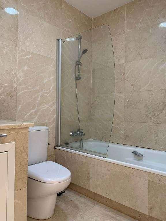 Badezimmer mit Badewanne, Duschabtrennung und wandhängendem WC, gefliest in Beige.