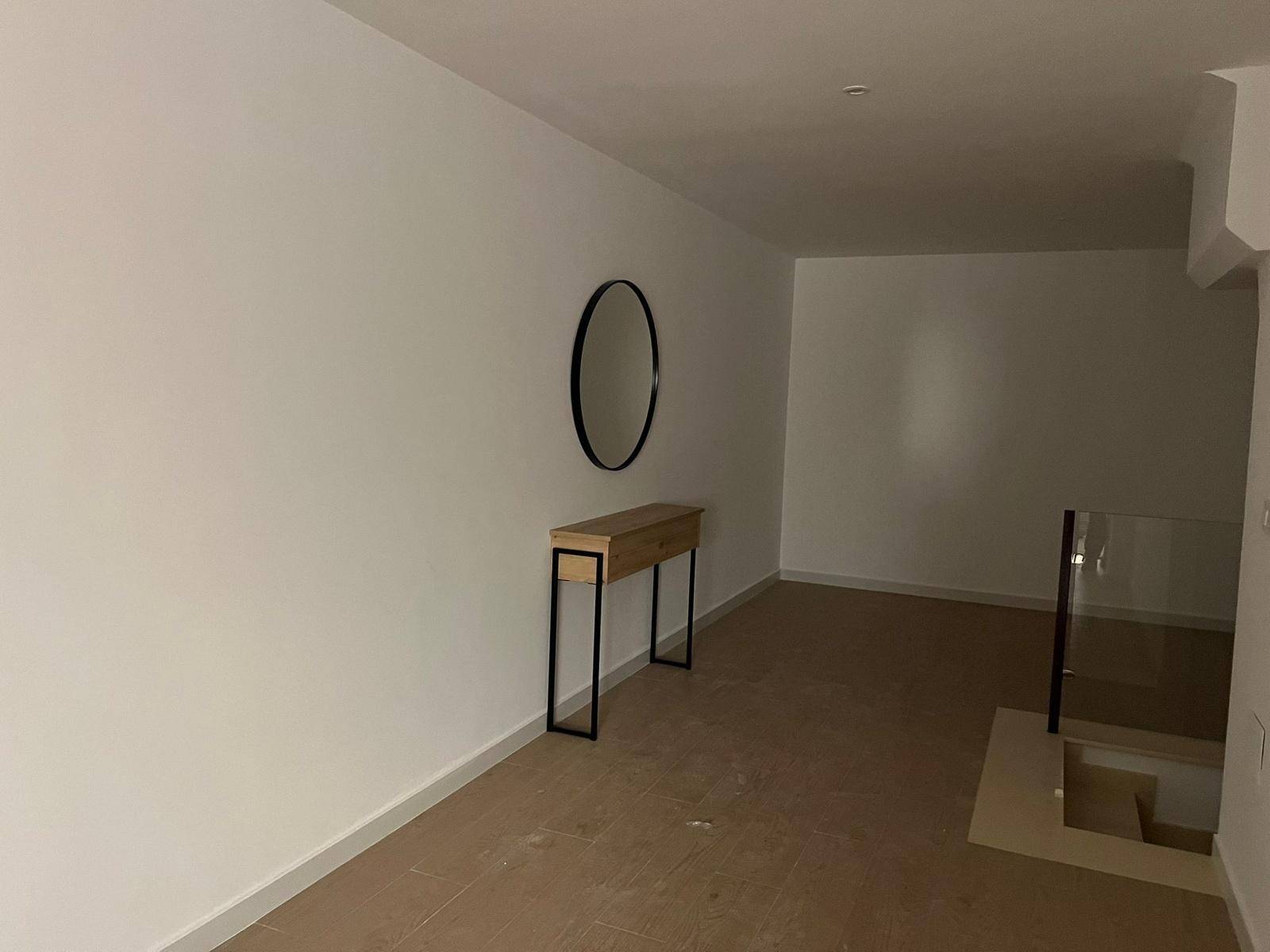 Heller Flur mit minimalistischer Konsole, ovalem Spiegel und Treppenabgang mit Glasgeländer.