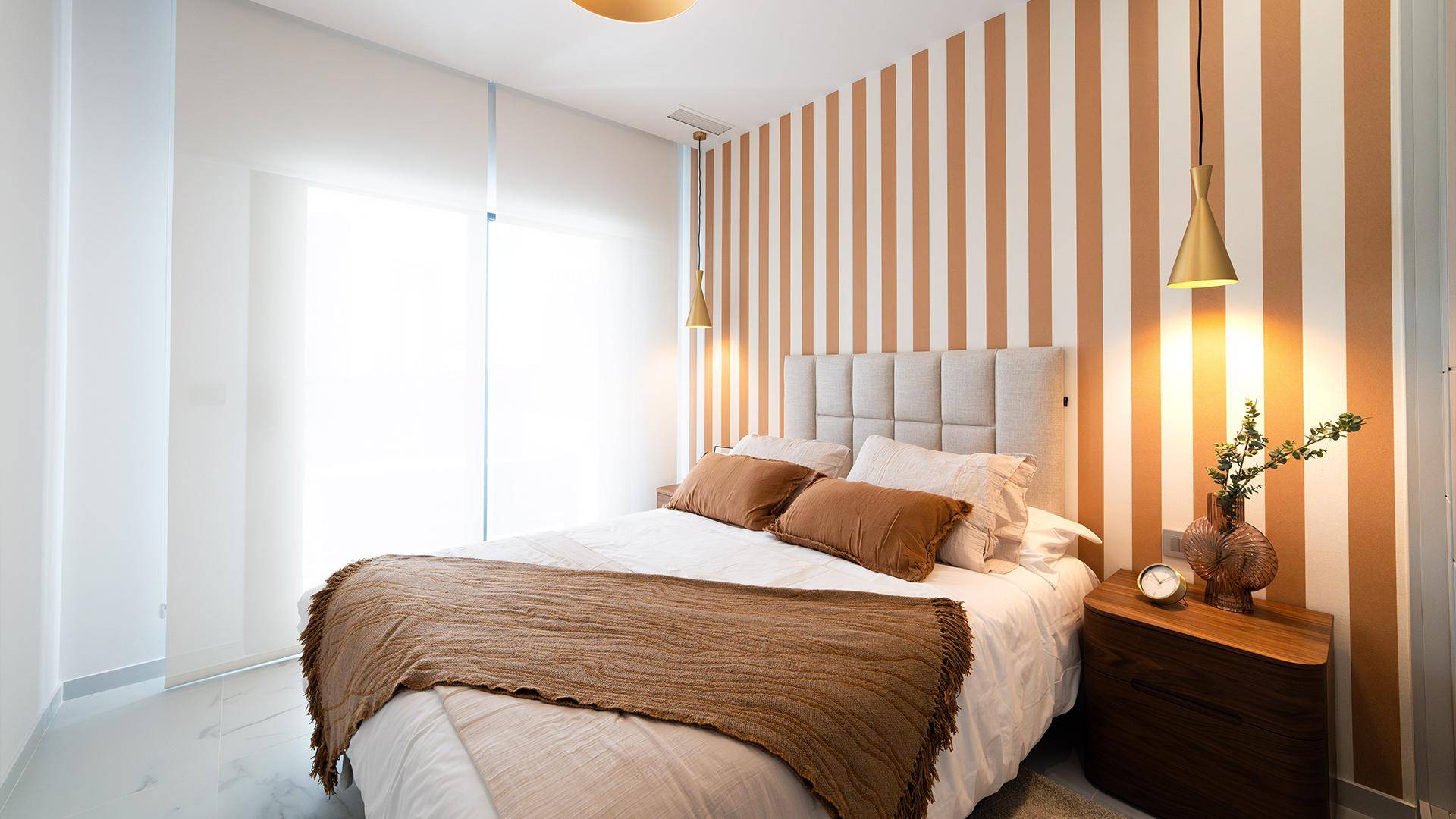 Modernes Schlafzimmer mit Doppelbett, gestreifter Wand und warmen Farbakzenten.