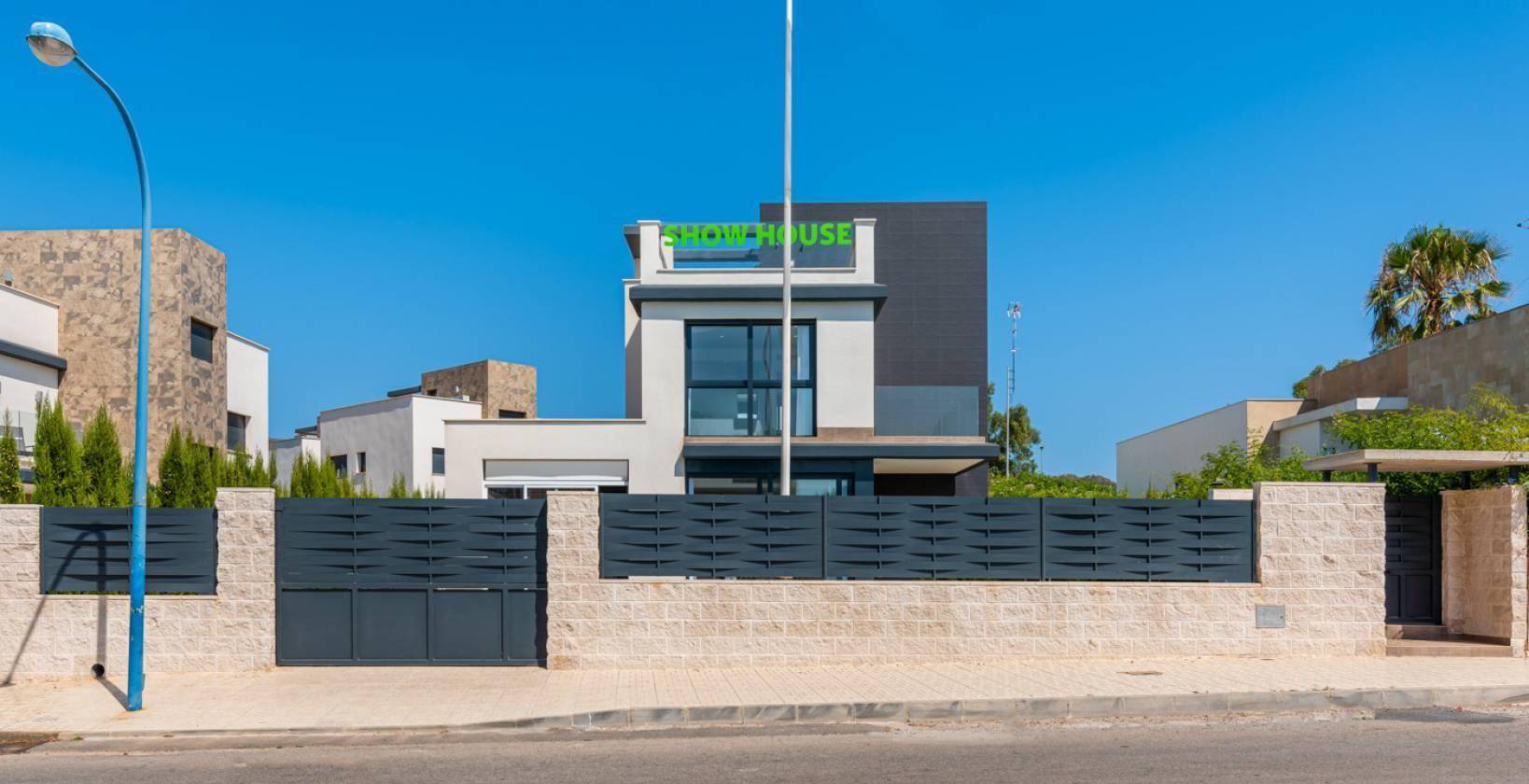 Moderne Villa von der Straße aus gesehen mit eleganter Zaunanlage und klarem Himmel.
