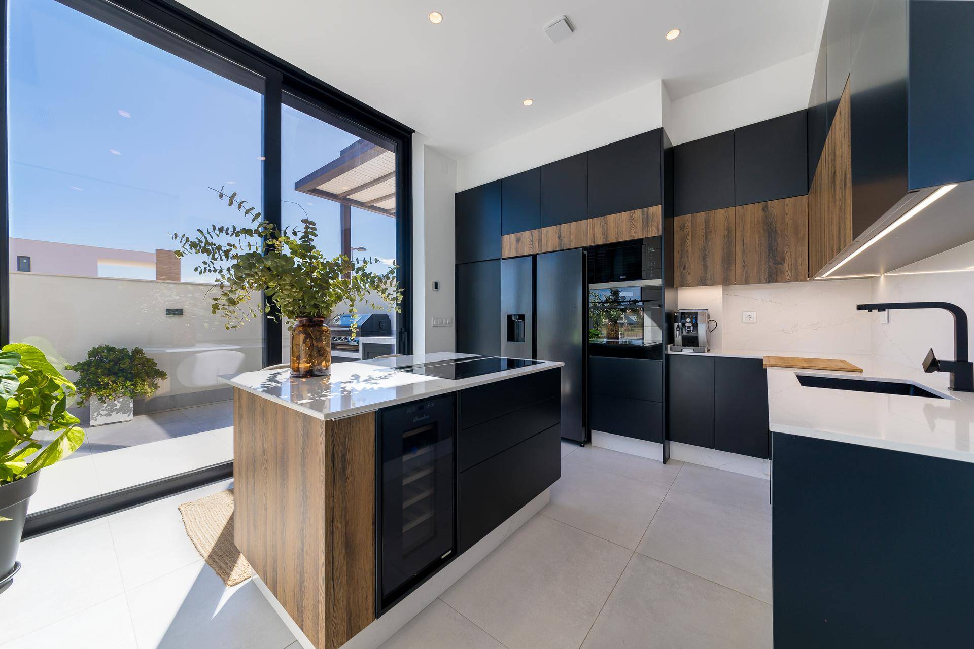 Moderne Küche mit dunklen Schränken, Holzdetails und heller Arbeitsplatte, mit Zugang zur Terrasse.