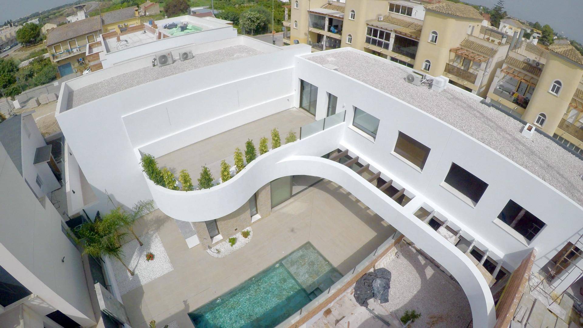 Weitläufige Luftaufnahme der modernen Villa mit geschwungener Architektur und begrünter Dachterrasse in der Nachbarschaft.