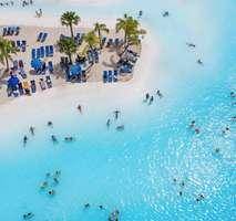 Luftaufnahme der belebten Lagune mit Badegästen, Sandstrand und Liegestühlen.