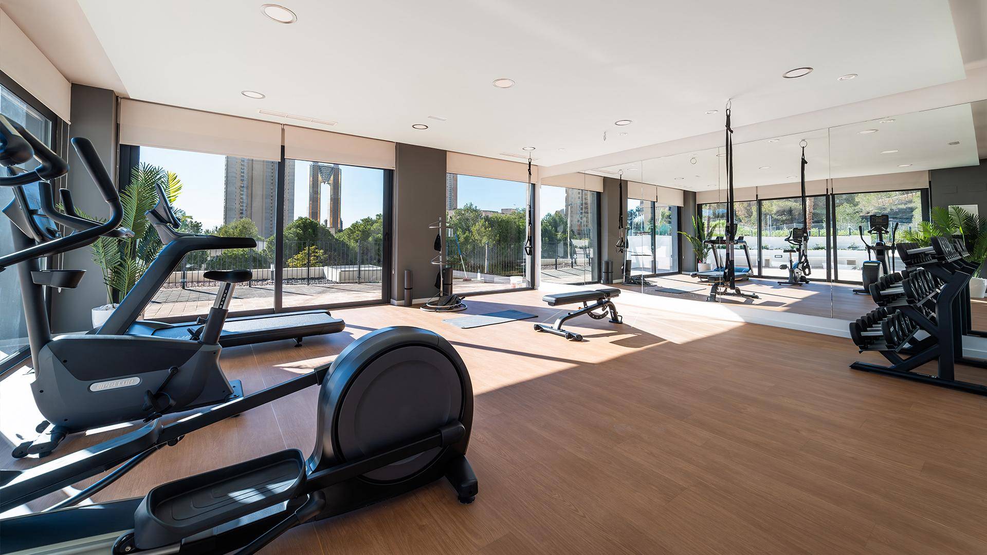 Heller Fitnessraum mit modernen Trainingsgeräten und großen Fenstern mit Ausblick.