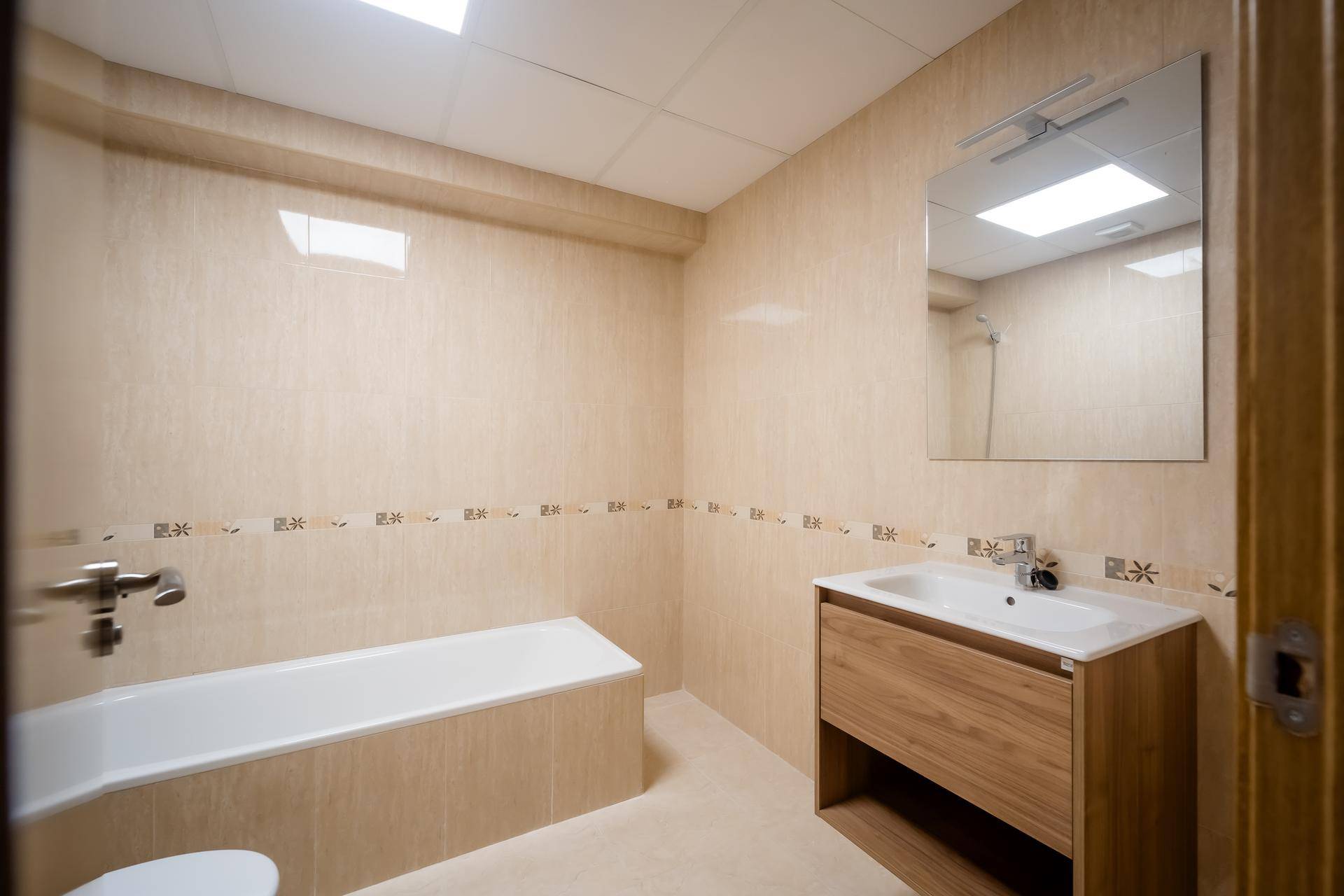 Badezimmer mit beigefarbenen Fliesen, Badewanne und modernem Waschtischunterschrank.