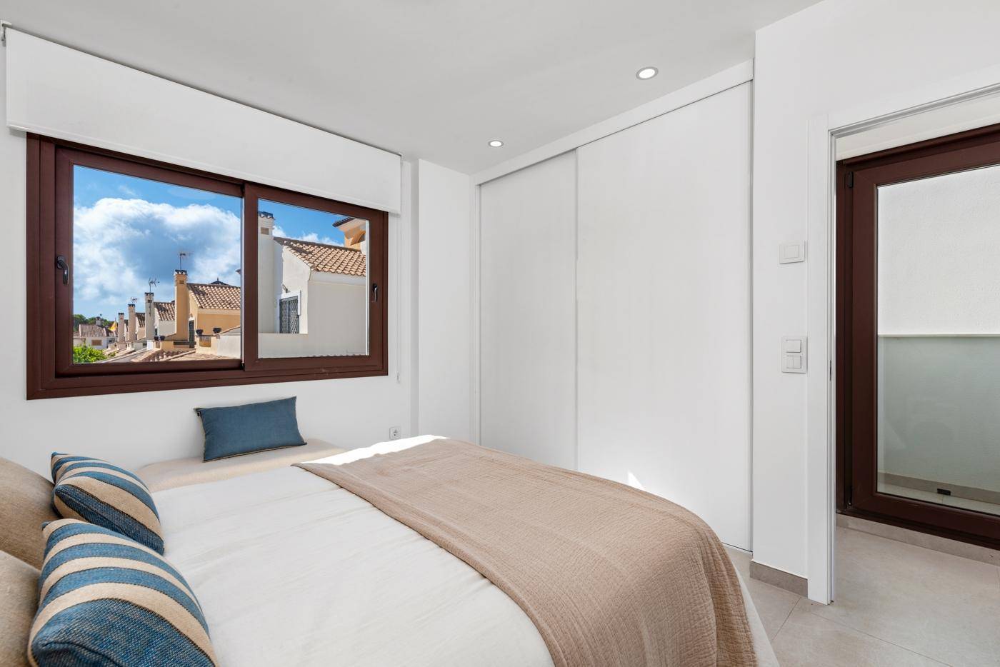 Helles Schlafzimmer mit Doppelbett, Einbauschrank und Fenster mit Blick auf die Nachbarschaft.