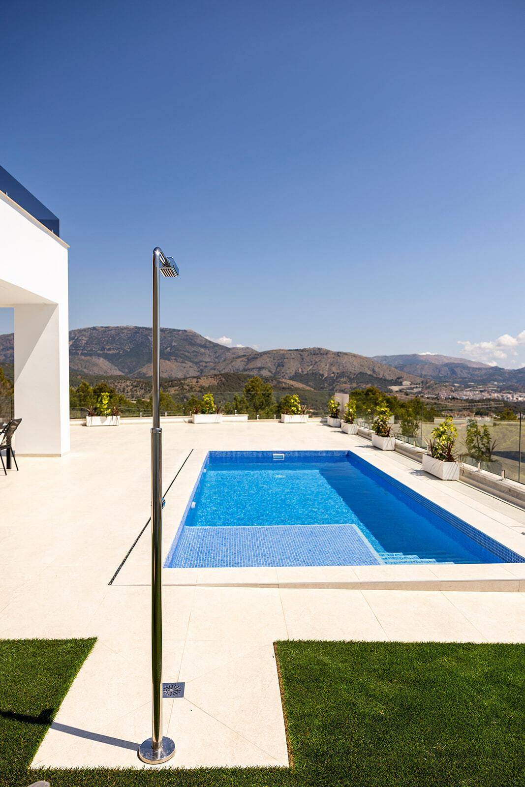 Sonniger Poolbereich mit blauen Mosaikfliesen, Außendusche und Bergblick.