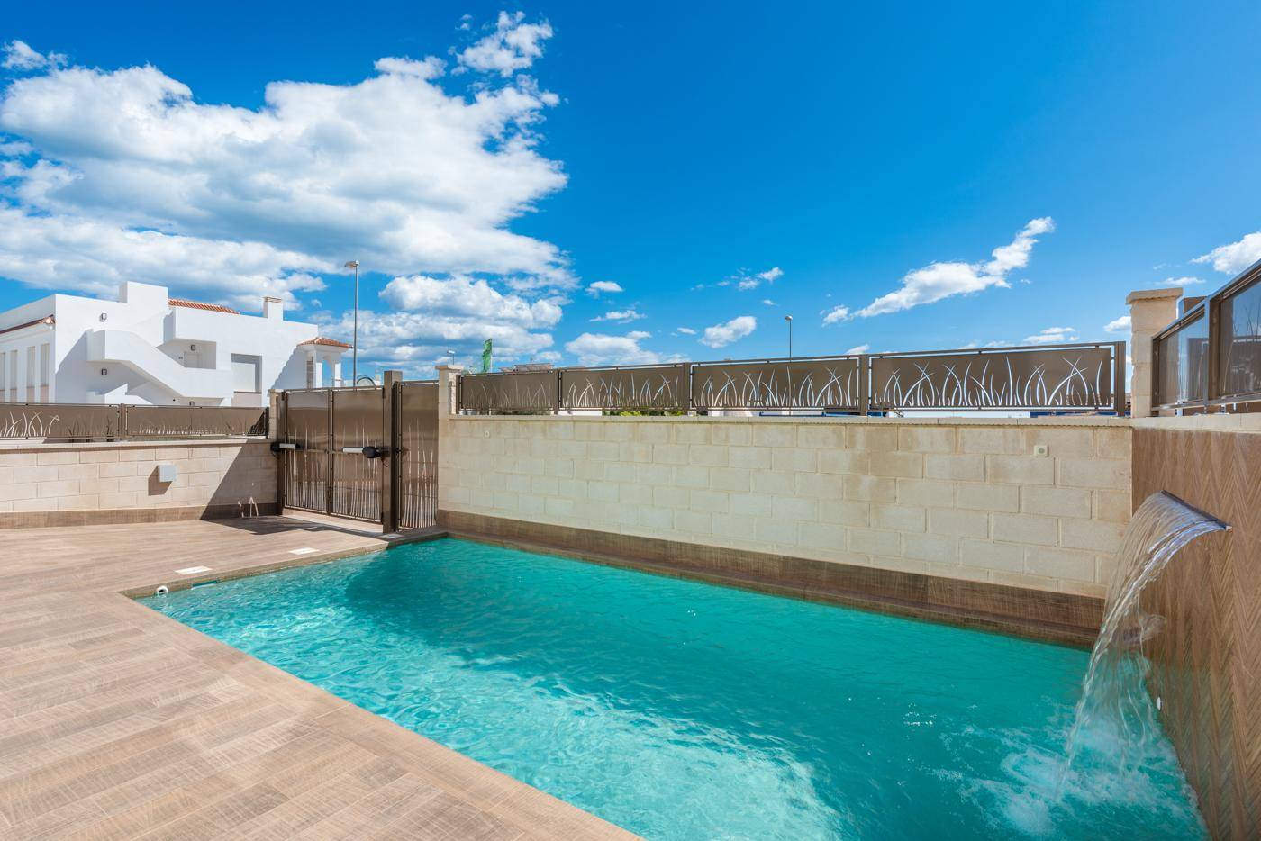 Privater Poolbereich mit Wasserfall und Zugangstor, umgeben von modernen Terrassenfliesen und Mauern.