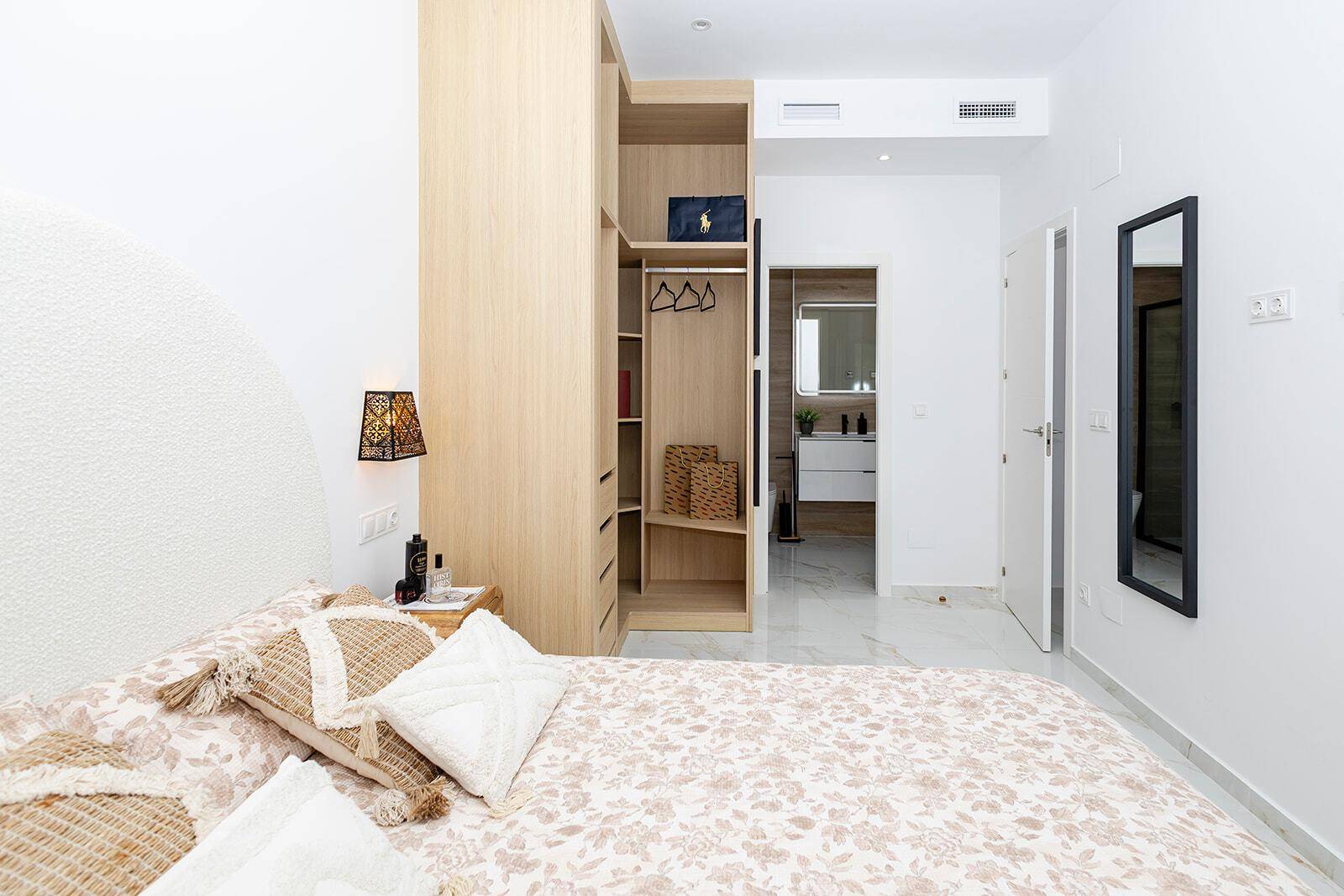 Helles Schlafzimmer mit Doppelbett, offenem Kleiderschrank und Zugang zum Badezimmer.