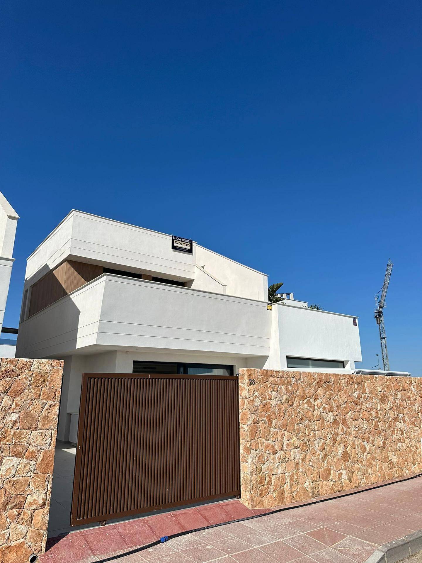 Moderne Hausfassade mit Natursteinmauer und braunem Eingangstor unter klarem Himmel.