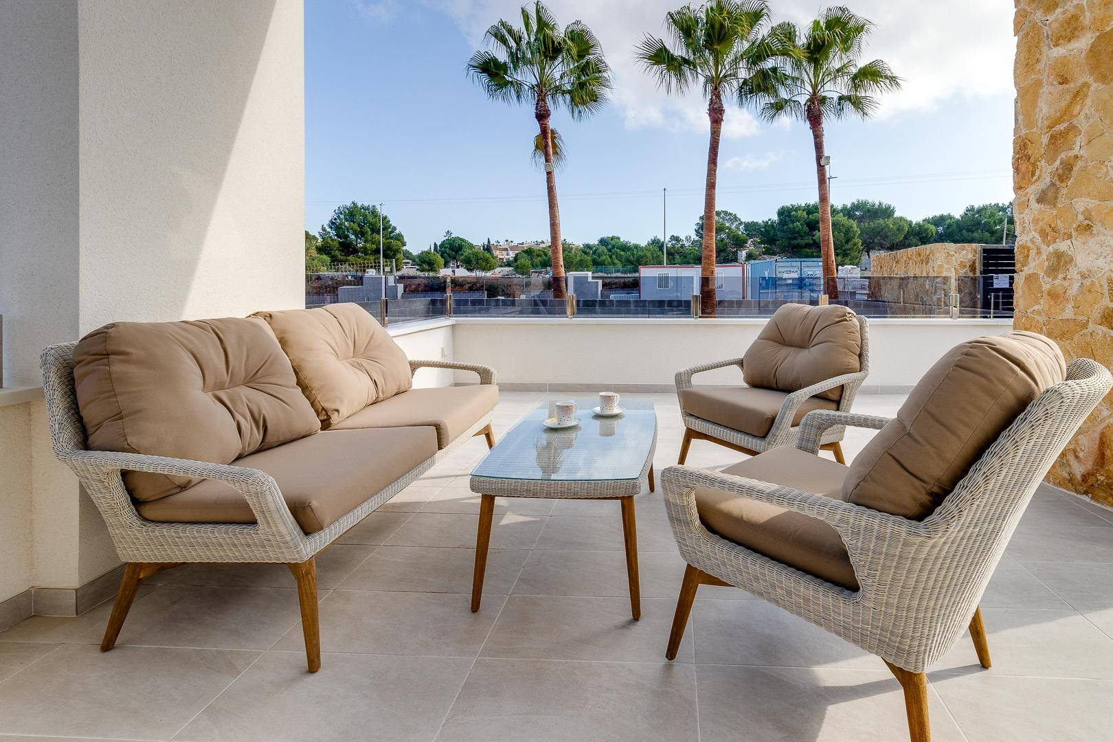 Gemütliche Terrasse mit modernen Outdoor-Möbeln und Blick auf Palmen unter blauem Himmel.
