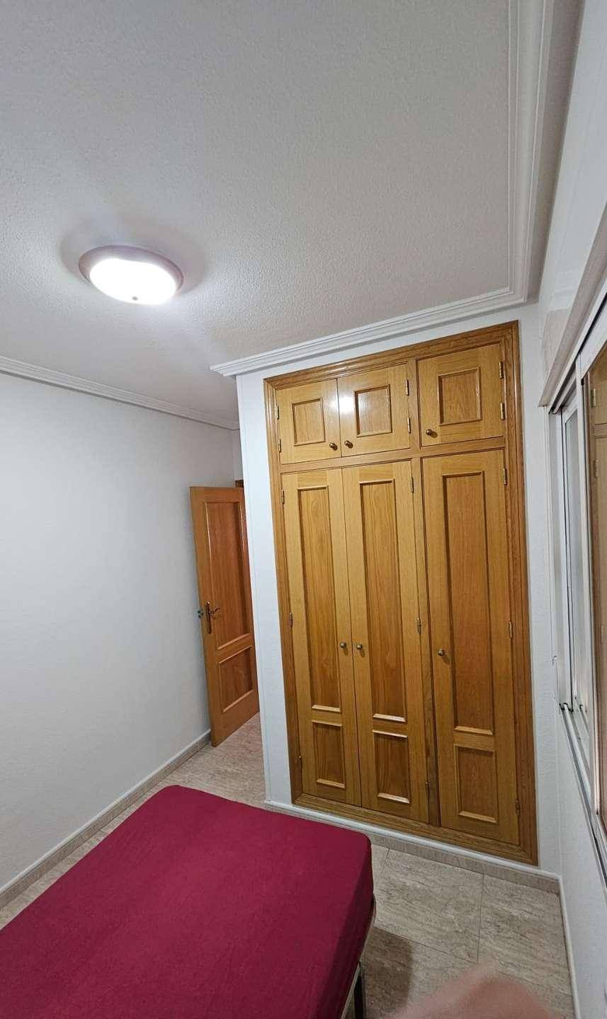 Schlafzimmer mit Einzelbett und großem Einbauschrank aus Holz.
