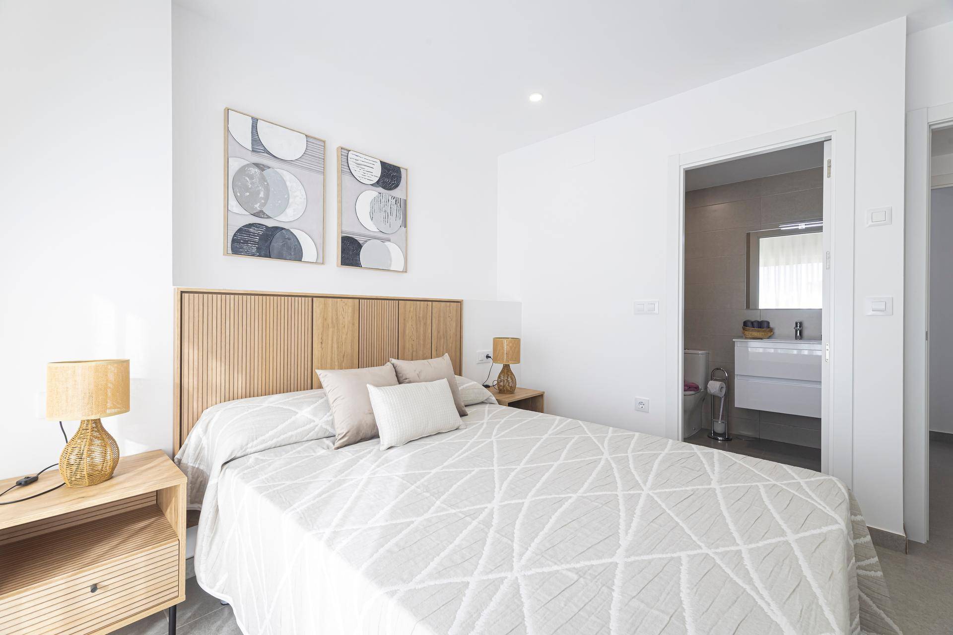 Helles Schlafzimmer mit Doppelbett, Holz-Kopfteil und Zugang zu einem angrenzenden Badezimmer.
