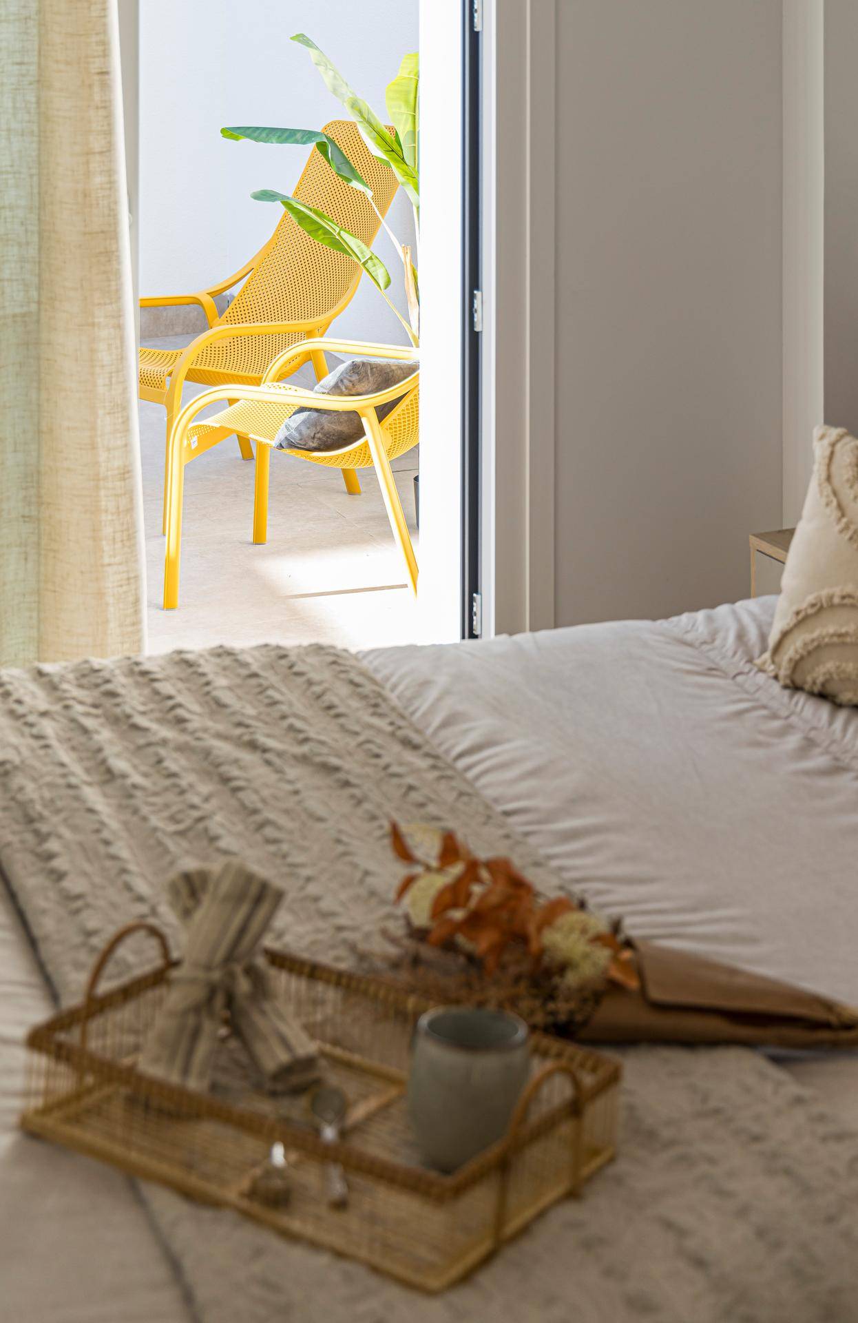 Schlafzimmer mit Blick auf den Balkon, der mit modernen gelben Liegestühlen ausgestattet ist.