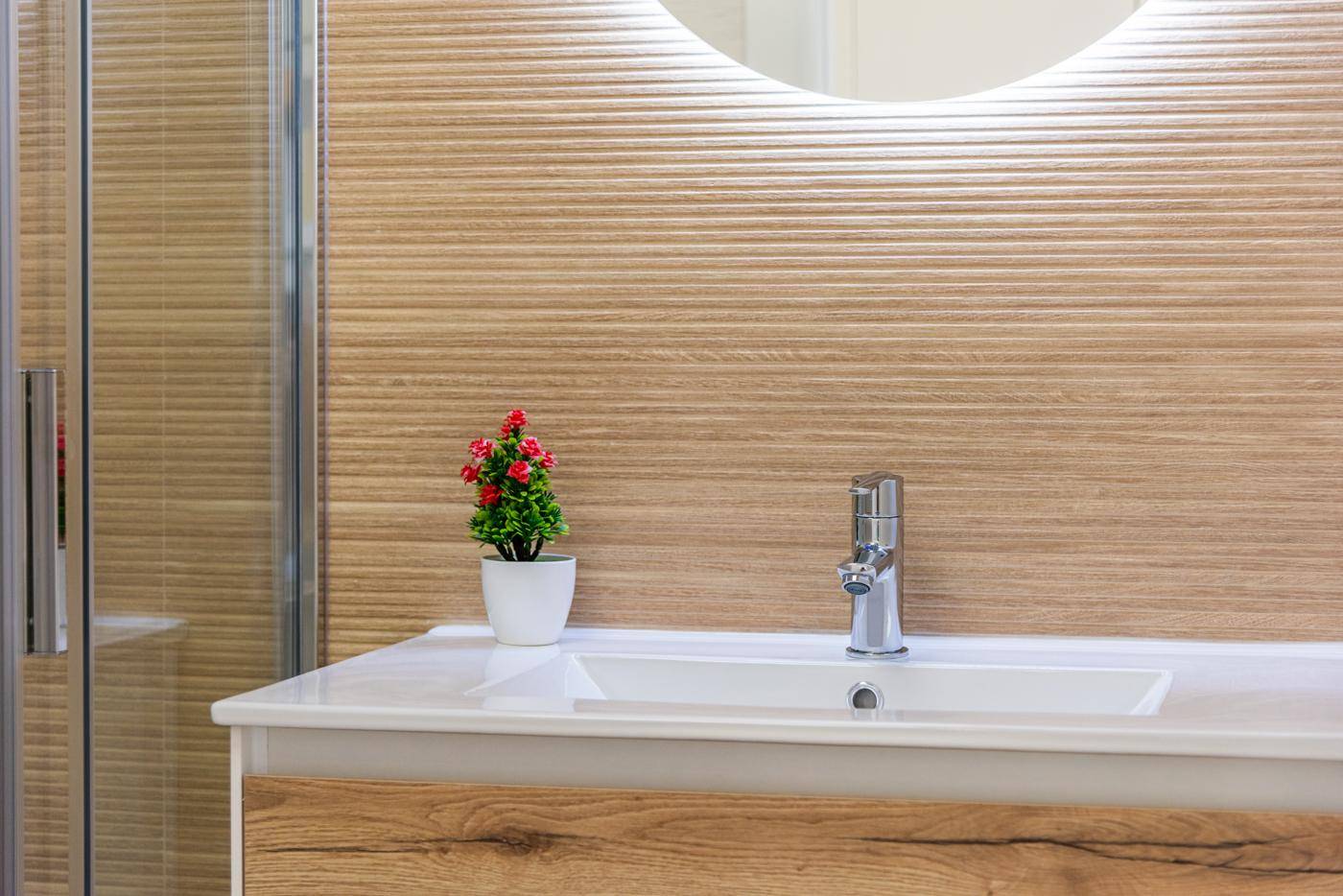 Modernes Badezimmer mit Einzelwaschbecken, Holzoptik-Fliesen und beleuchtetem Spiegel.