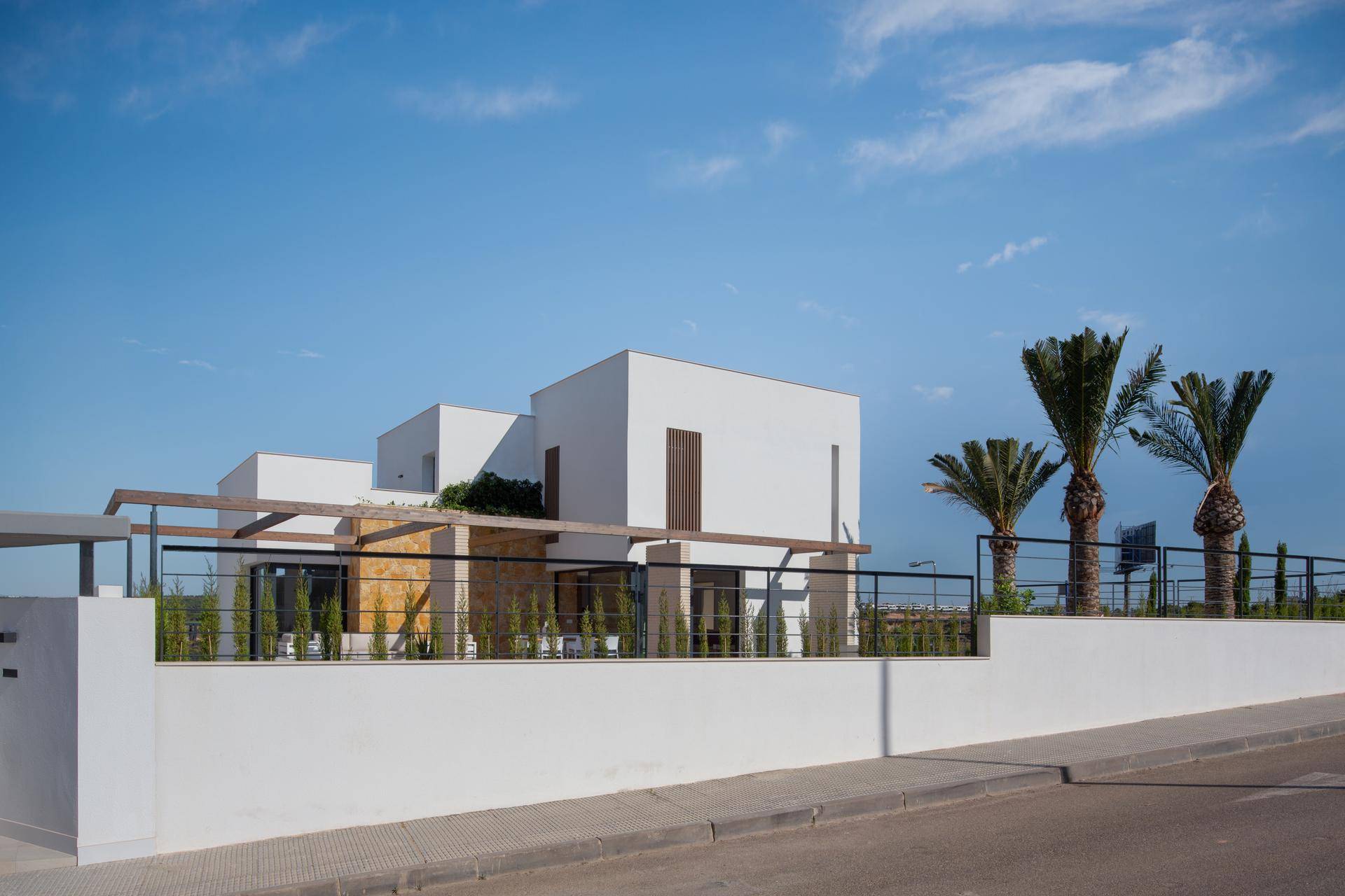 Moderne weiße Villa von der Straße aus gesehen mit eleganter Umzäunung und tropischen Palmen.