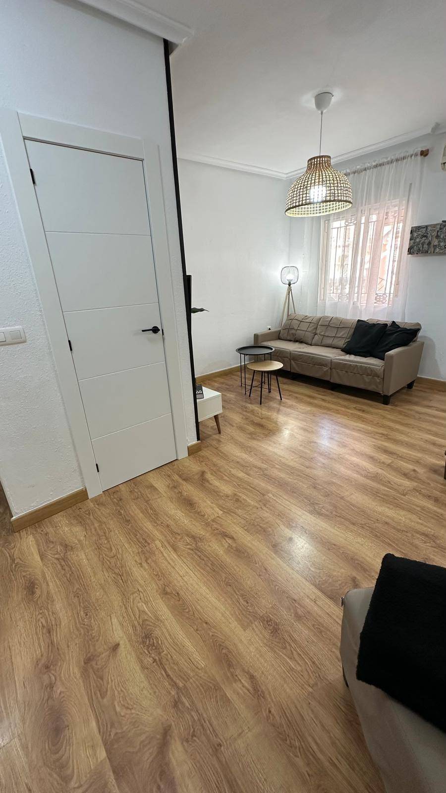 Helles Wohnzimmer mit beigem Sofa, Holzboden und modernen Beistelltischen.
