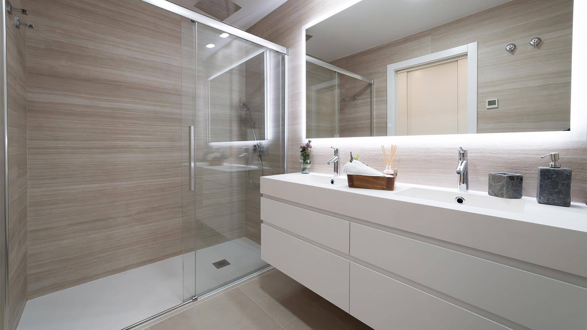 Modernes Badezimmer mit Doppelwaschbecken, beleuchtetem Spiegel und begehbarer Dusche.