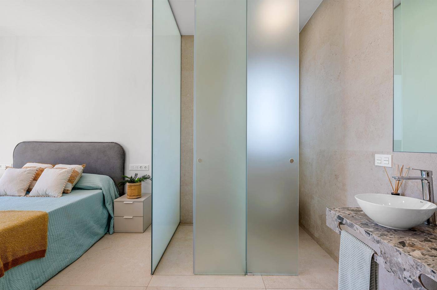 Schlafzimmer mit durchscheinenden Schiebetüren zum modernen Badbereich und Einzelwaschbecken.