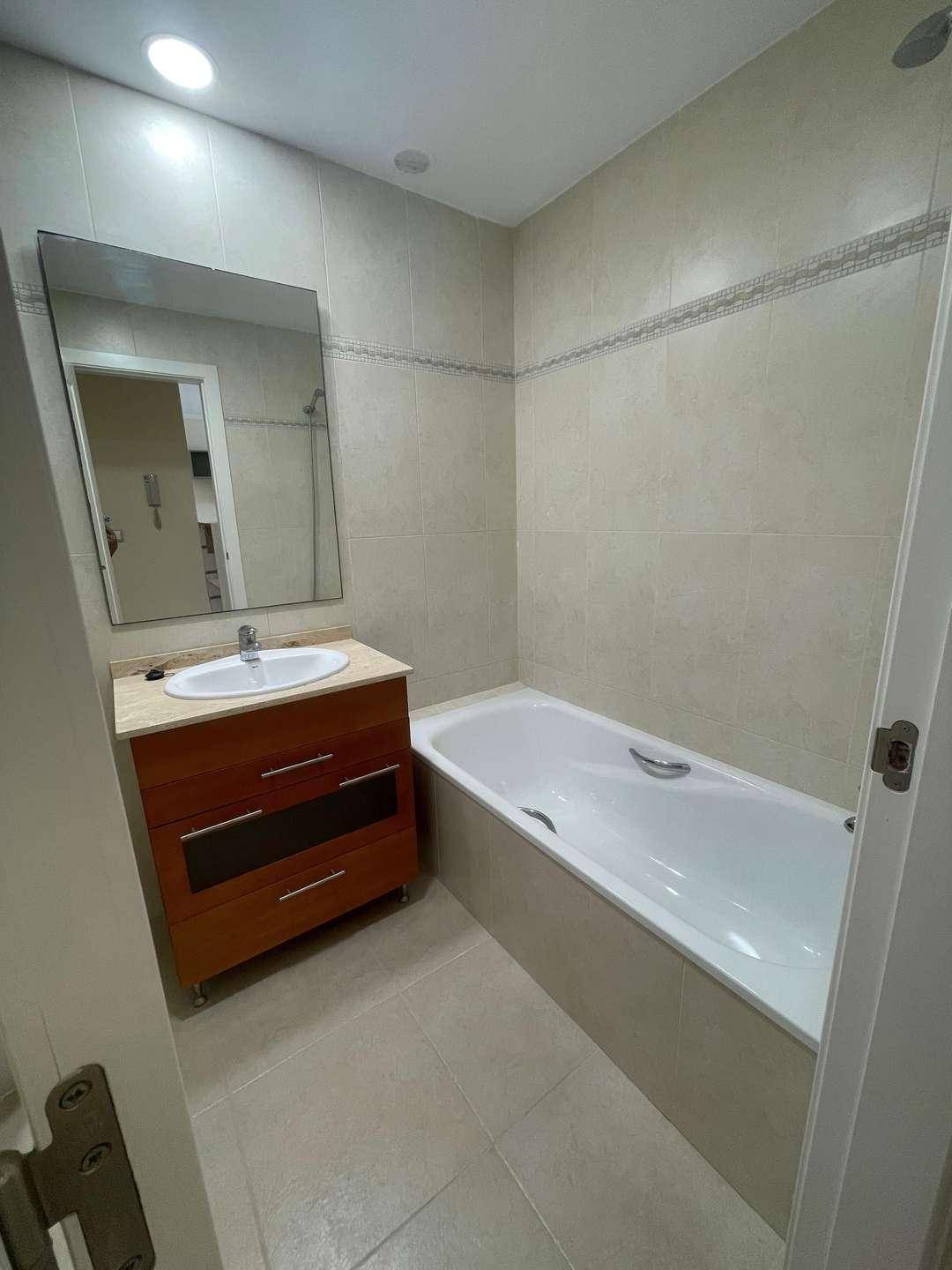 Modernes Badezimmer mit Badewanne, Einzelwaschbecken und großem Spiegel, komplett gefliest.