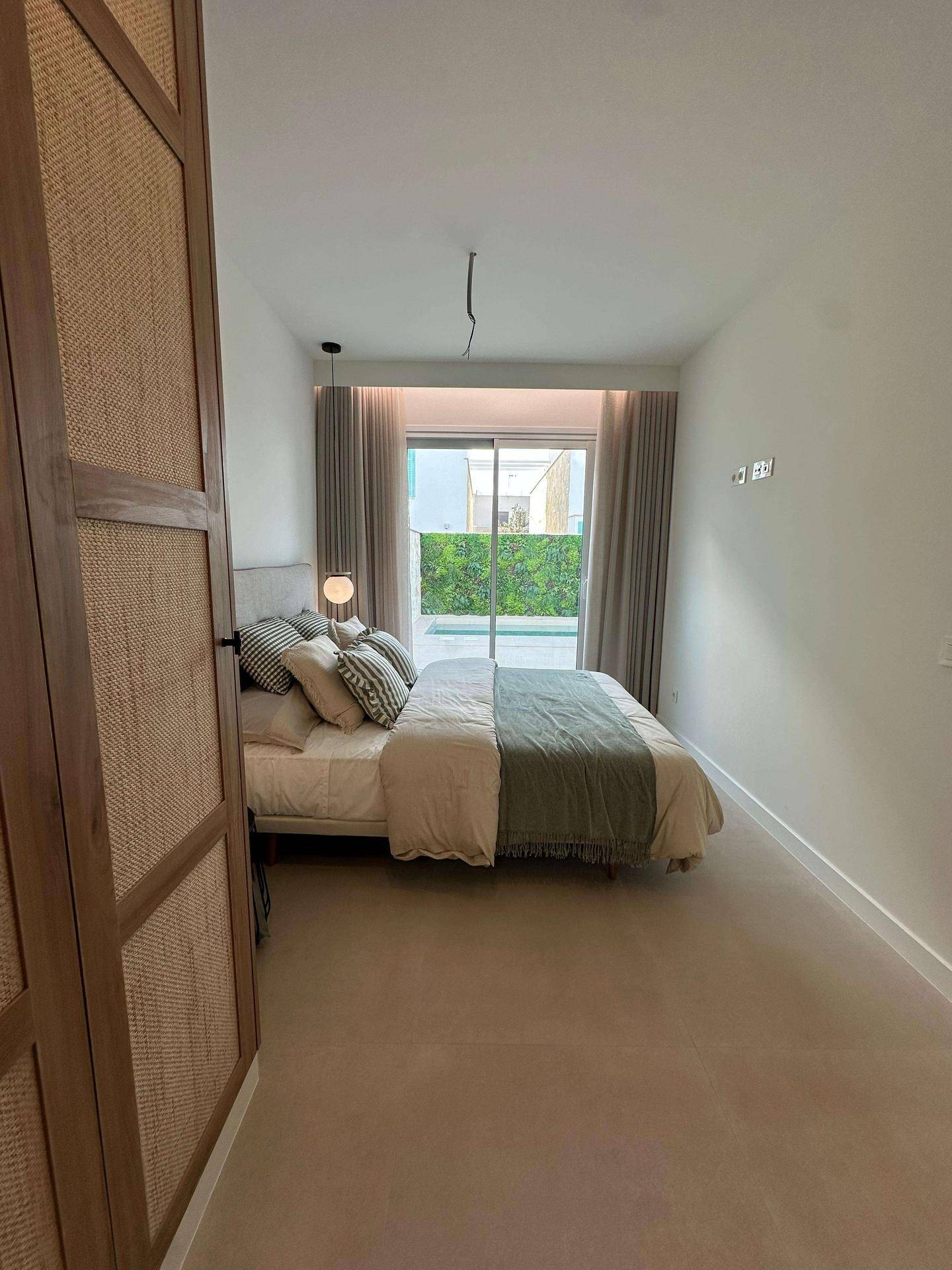 Helles Schlafzimmer mit Doppelbett, Rattanschränken und großen Fenstern mit Blick ins Grüne.