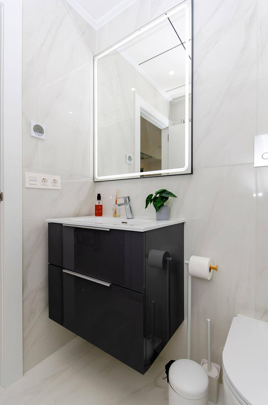 Modernes Badezimmer mit beleuchtetem Spiegel, schwebendem Waschtisch und eleganten Fliesen.