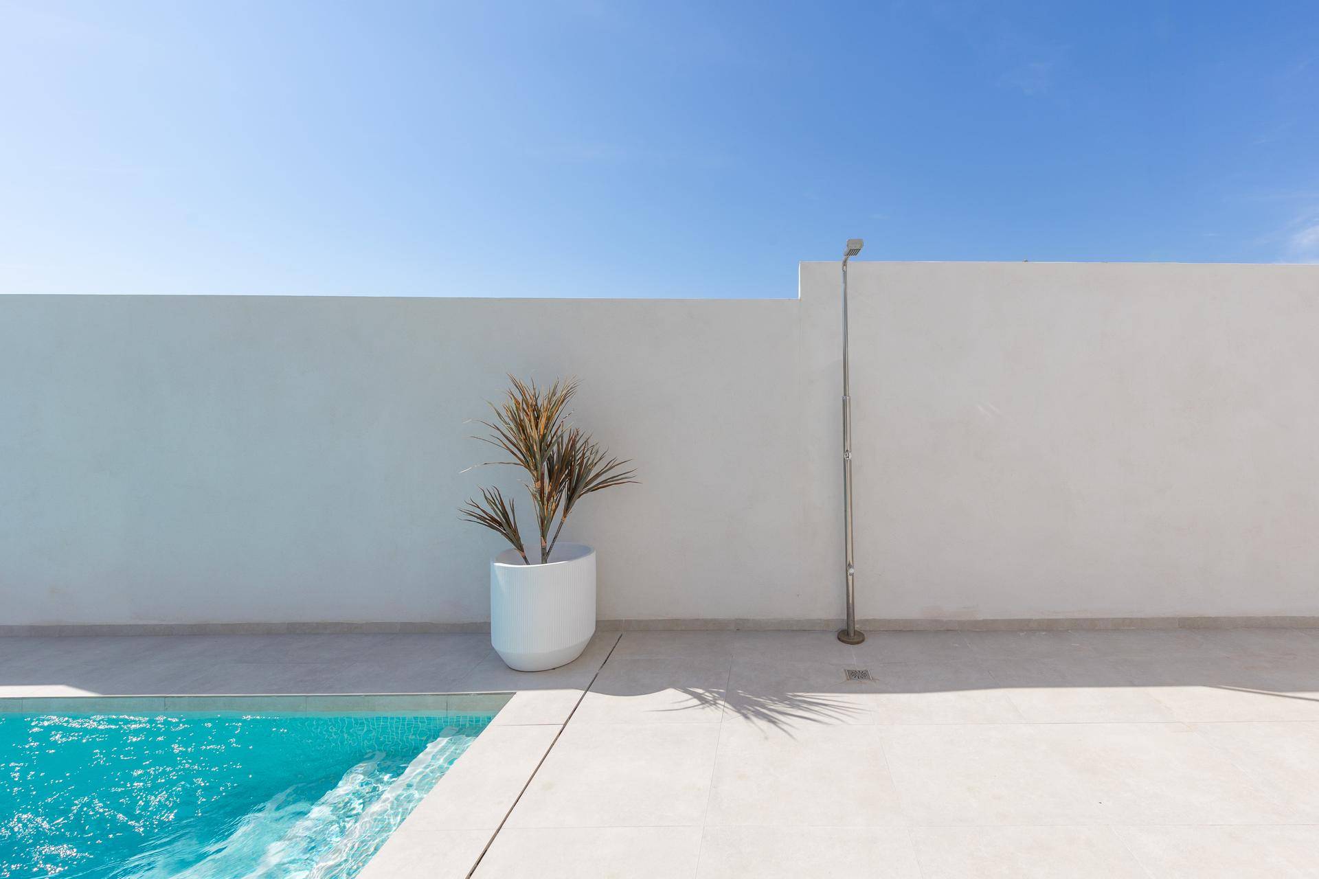 Minimalistischer Außenbereich mit Pool, weißer Mauer und Außendusche.