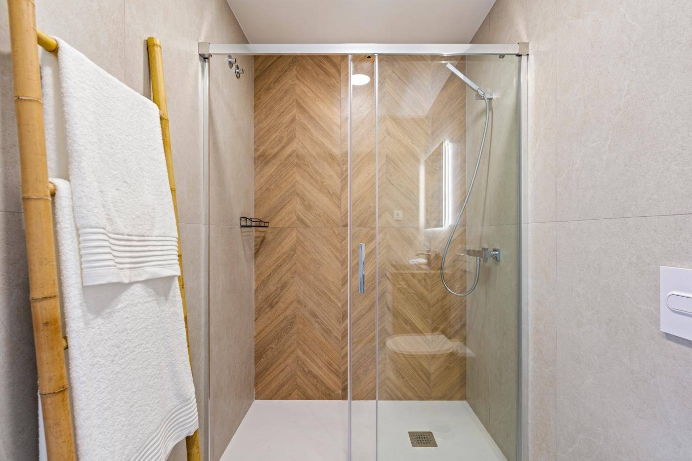 Modernes Badezimmer mit geräumiger Duschkabine und Holzmusterfliesen.