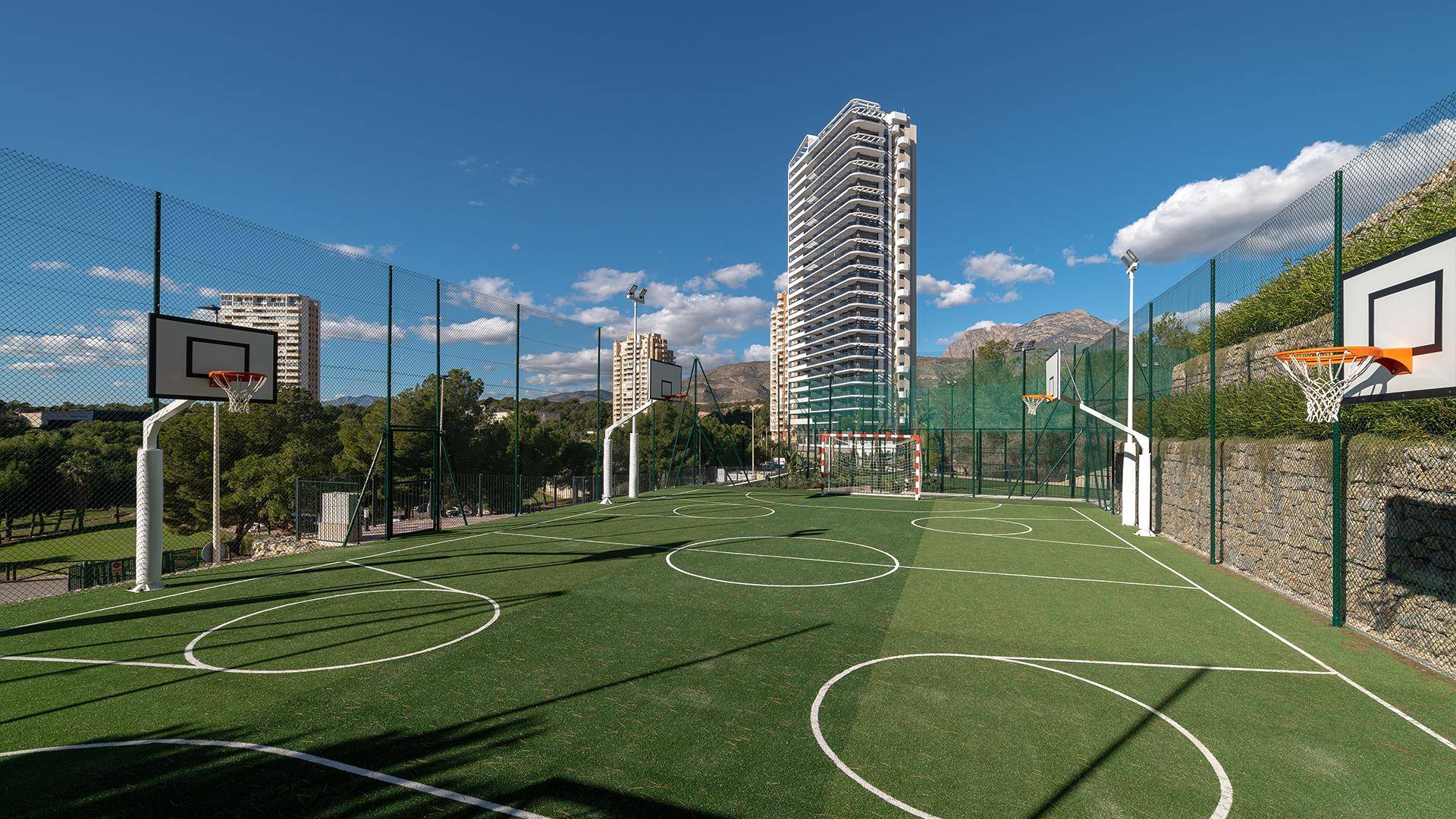 Outdoor-Sportplatz mit Basketballkörben und Kunstrasen, umgeben von grüner Landschaft.