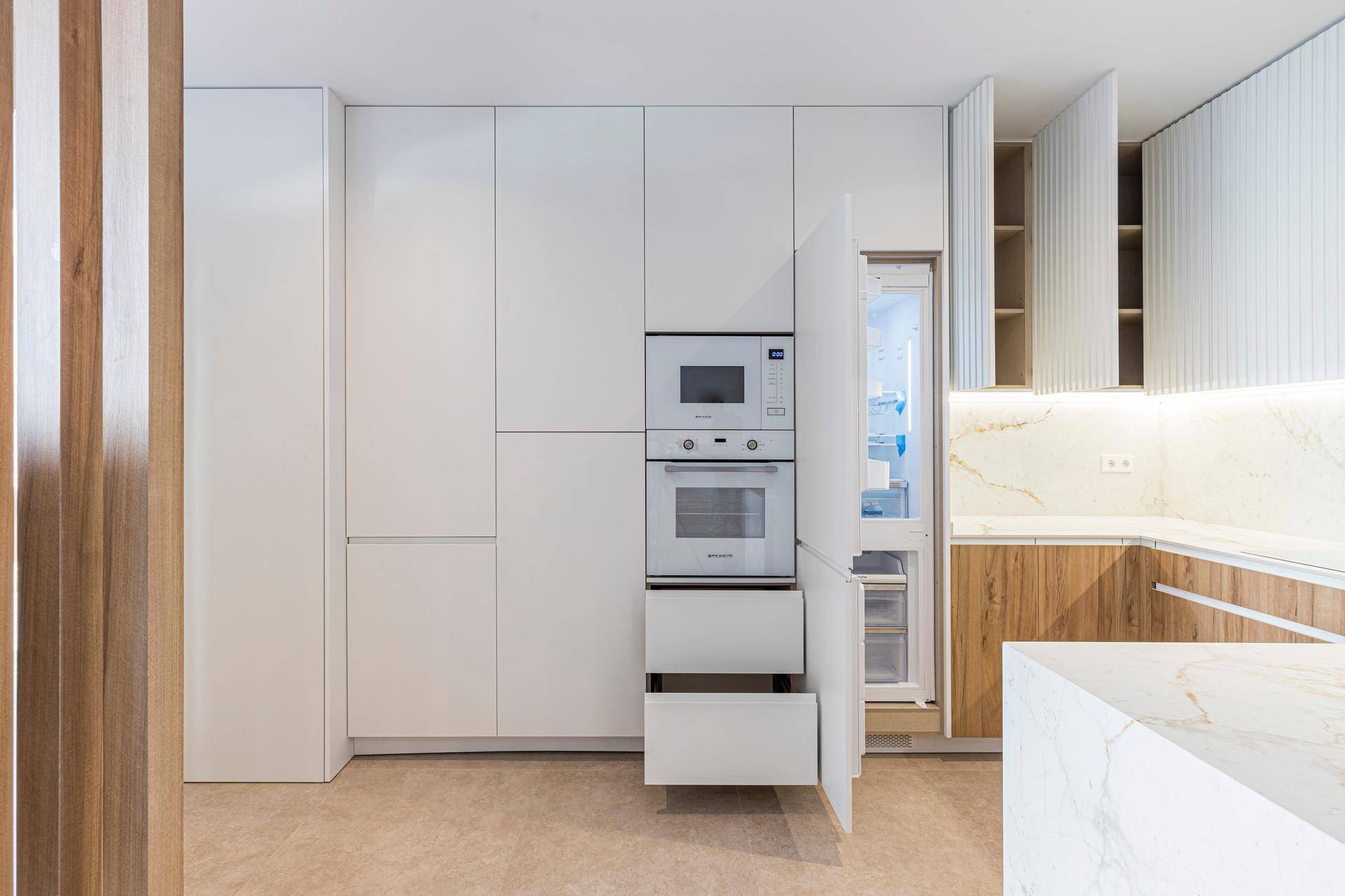 Moderne Einbauküche mit weißen Fronten, integrierten Geräten und eleganten Marmorarbeitsplatten.