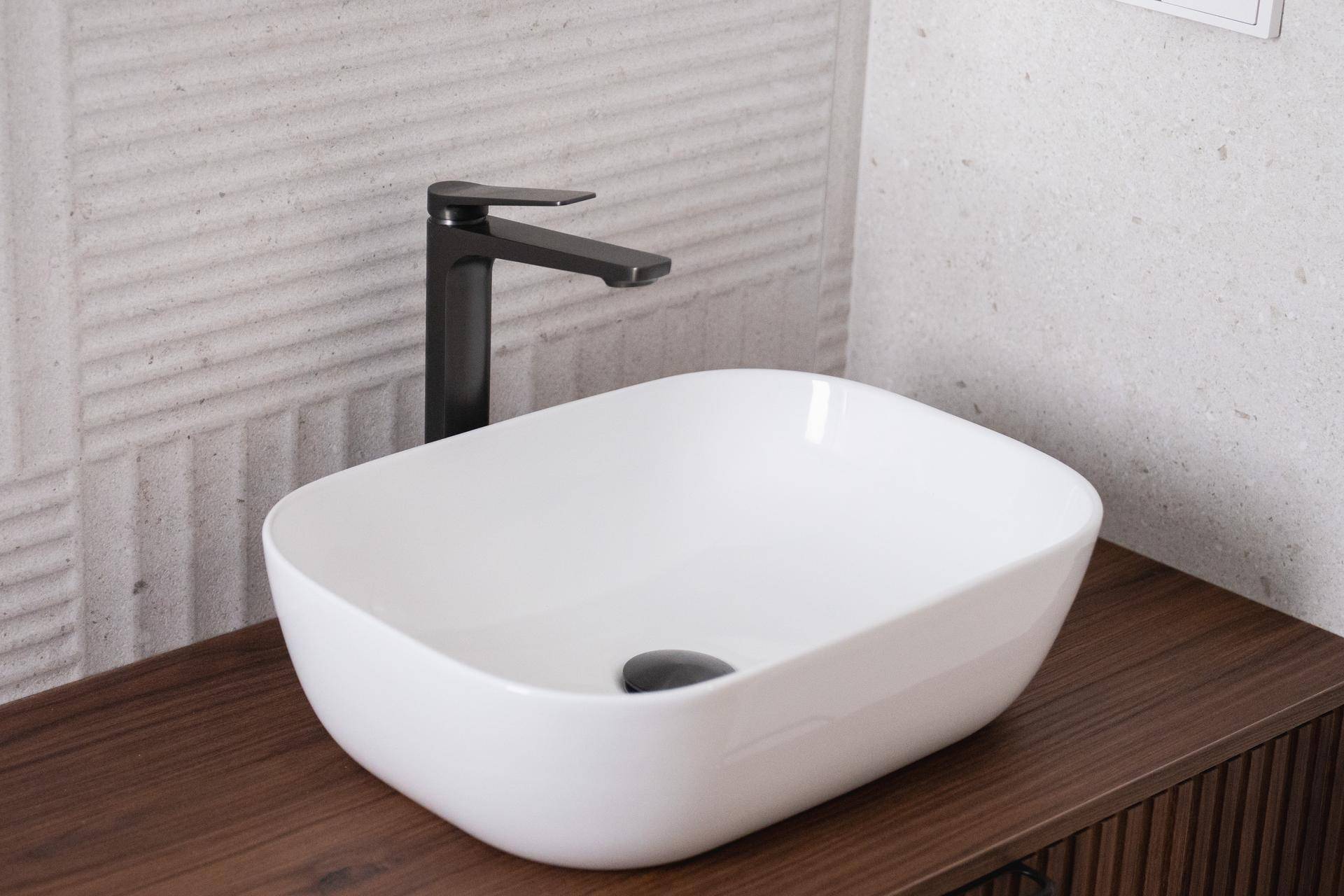 Moderner Aufsatzwaschtisch mit schwarzem Wasserhahn auf einem dunklen Holzunterschrank.