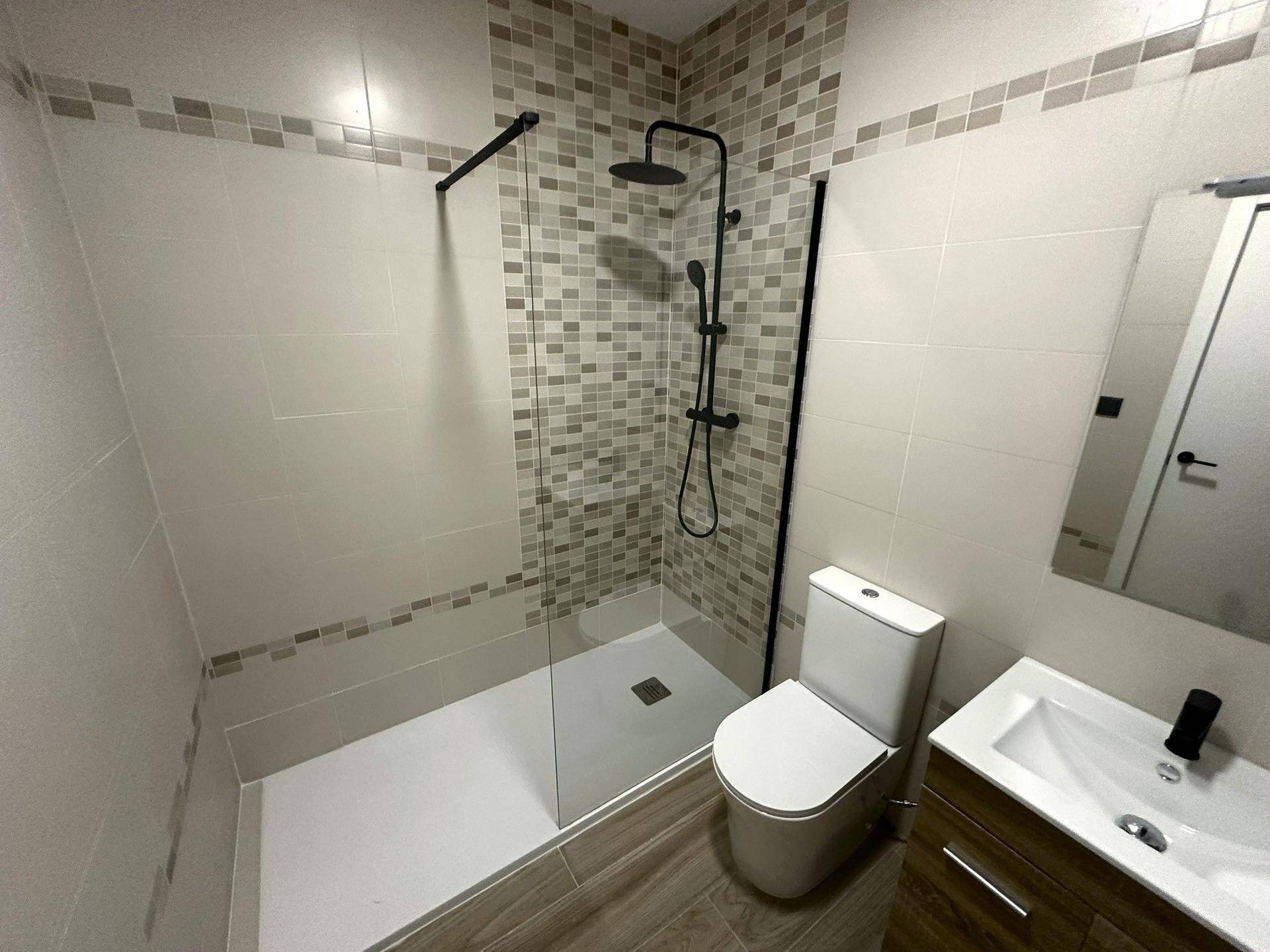 Modernes Badezimmer mit ebenerdiger Dusche, WC und Waschtisch, ausgestattet mit stilvollen Fliesen.